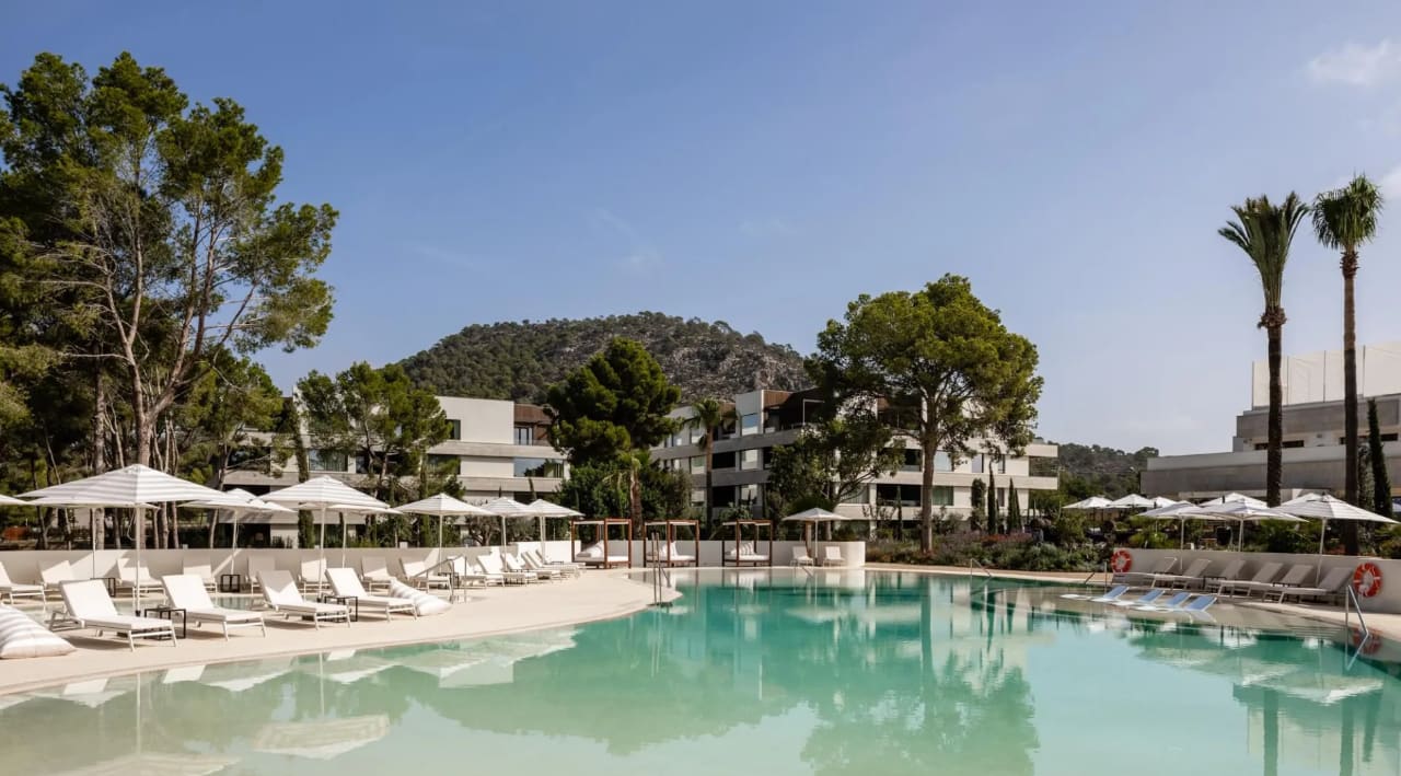 A hotel pool area with white loungers and umbrellas and a mountainous backdrop