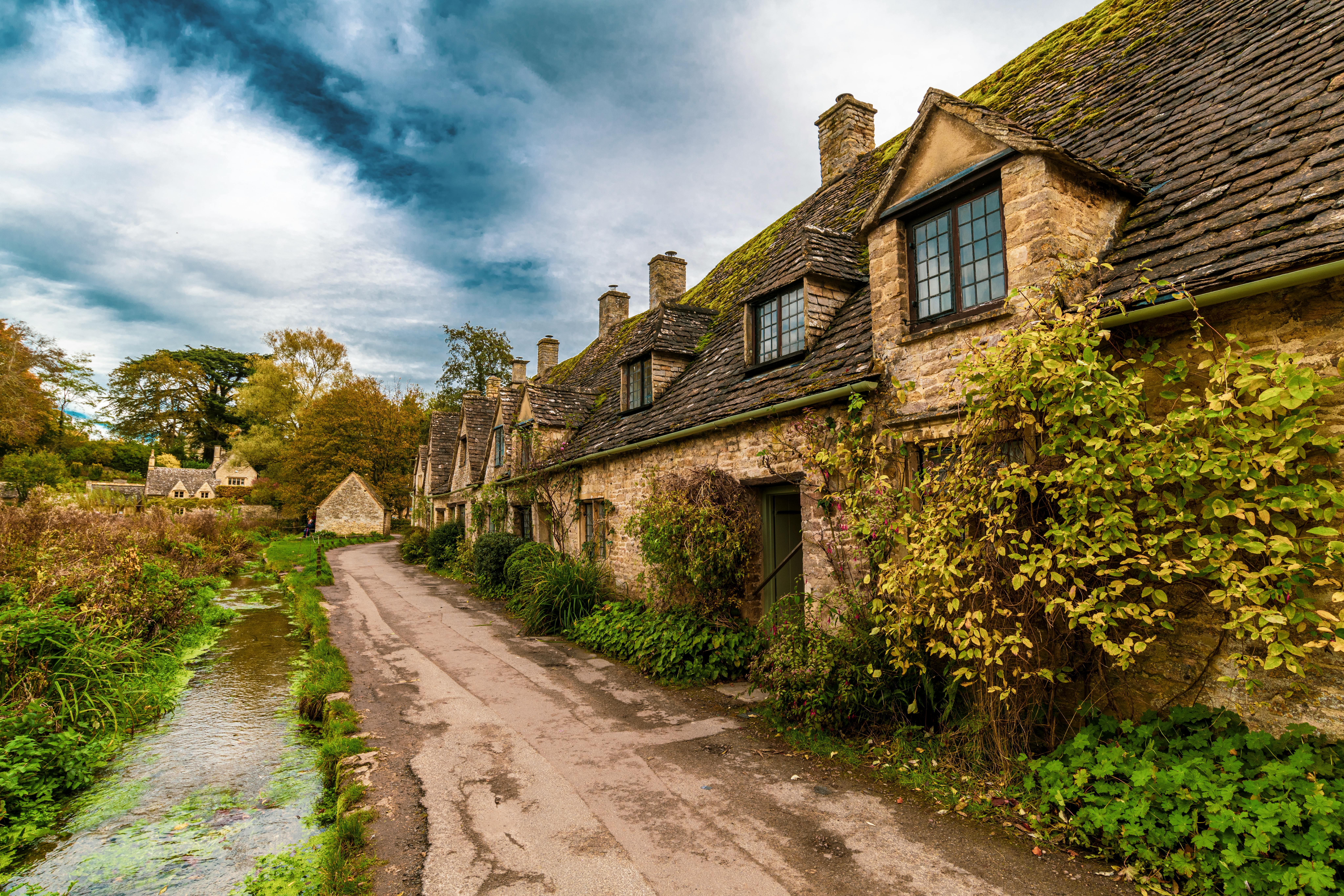 A creek next to a dirt path lining in front of old tan British homes during daytime