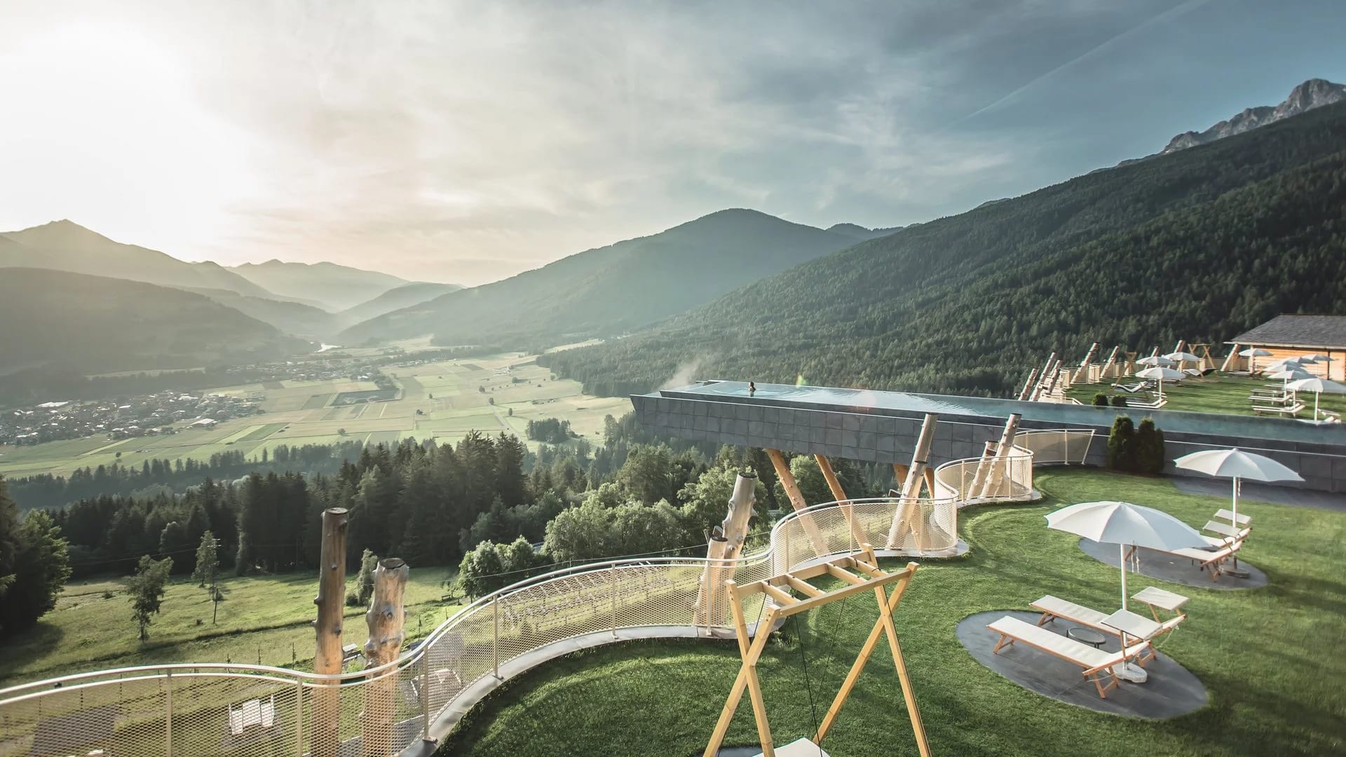 Aerial view of a conrete slab infinity pool extended out over a cliff with valley and mountain views