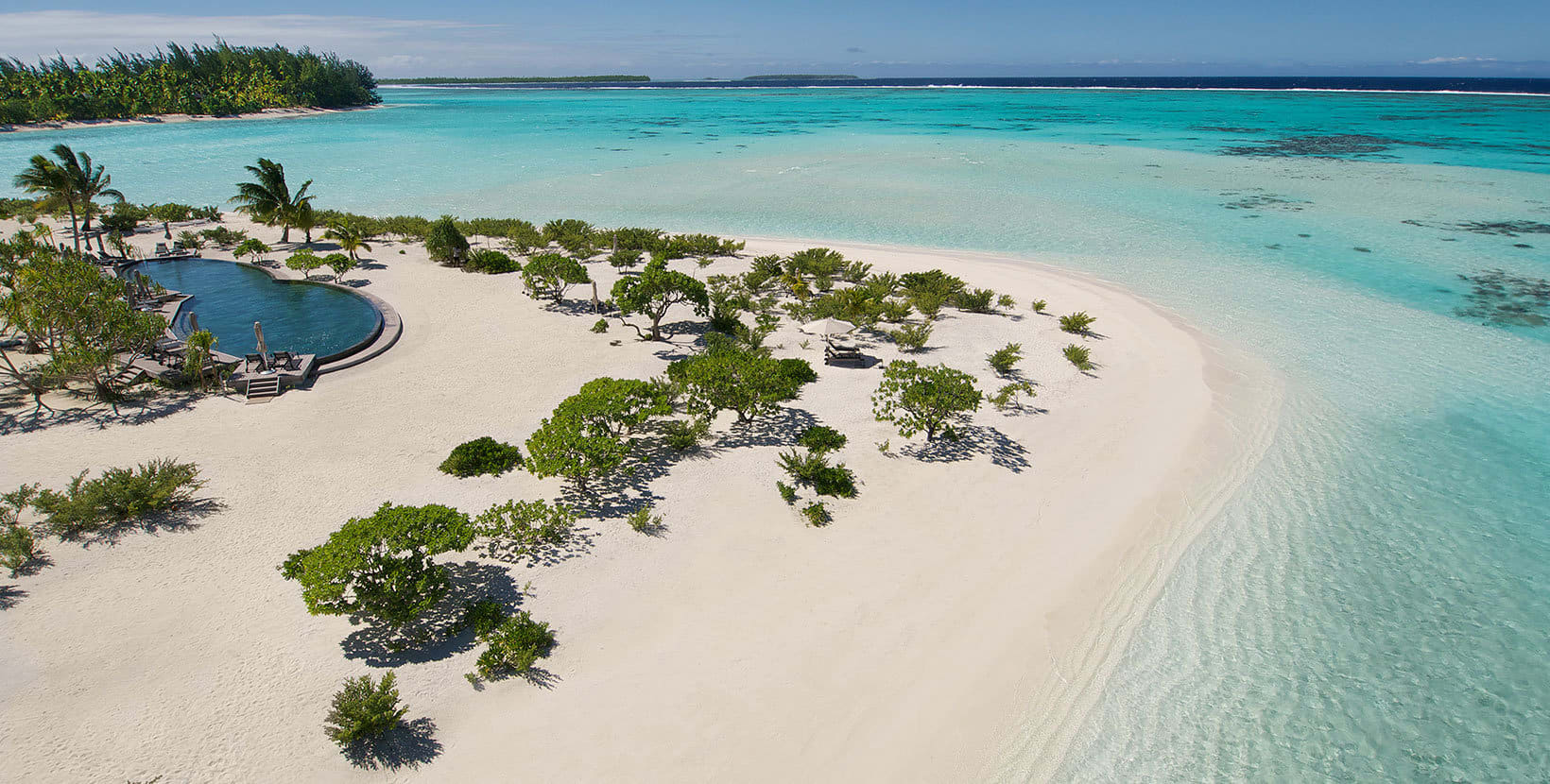 Aerial view of calm turquoise ocean, a white sand beach with some bushes, and a pool