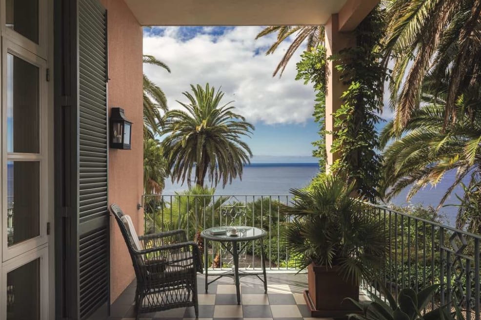 A hotel balcony view with the ocean as a backdrop and light pink walls