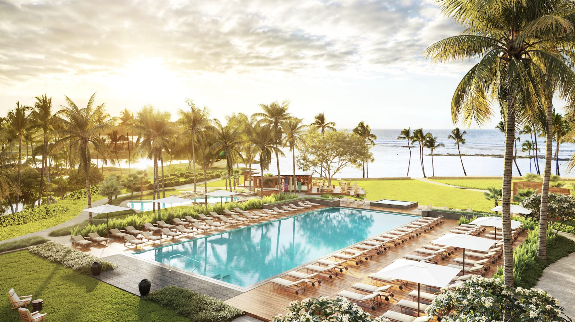 A hotel pool surrounded by lounge chairs and palm trees with the rising sun over the ocean in the distance