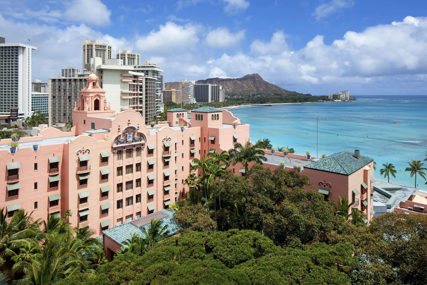 View of a retro pink building with green courtyard and ocean in the background during daytime