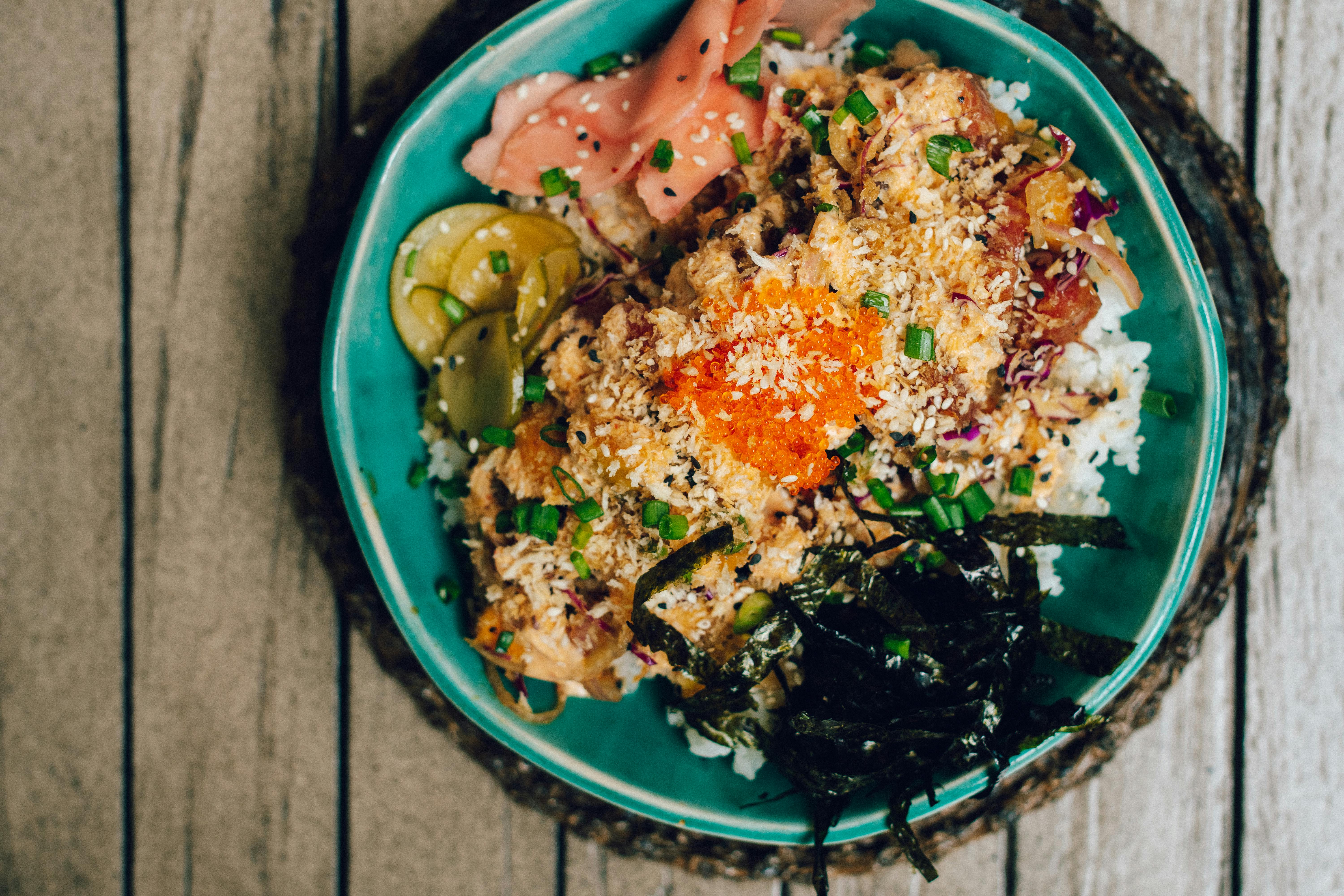 Overhead view of a poke bowl with rice, fish, seaweed and vegetables in a bowl on a wooden table