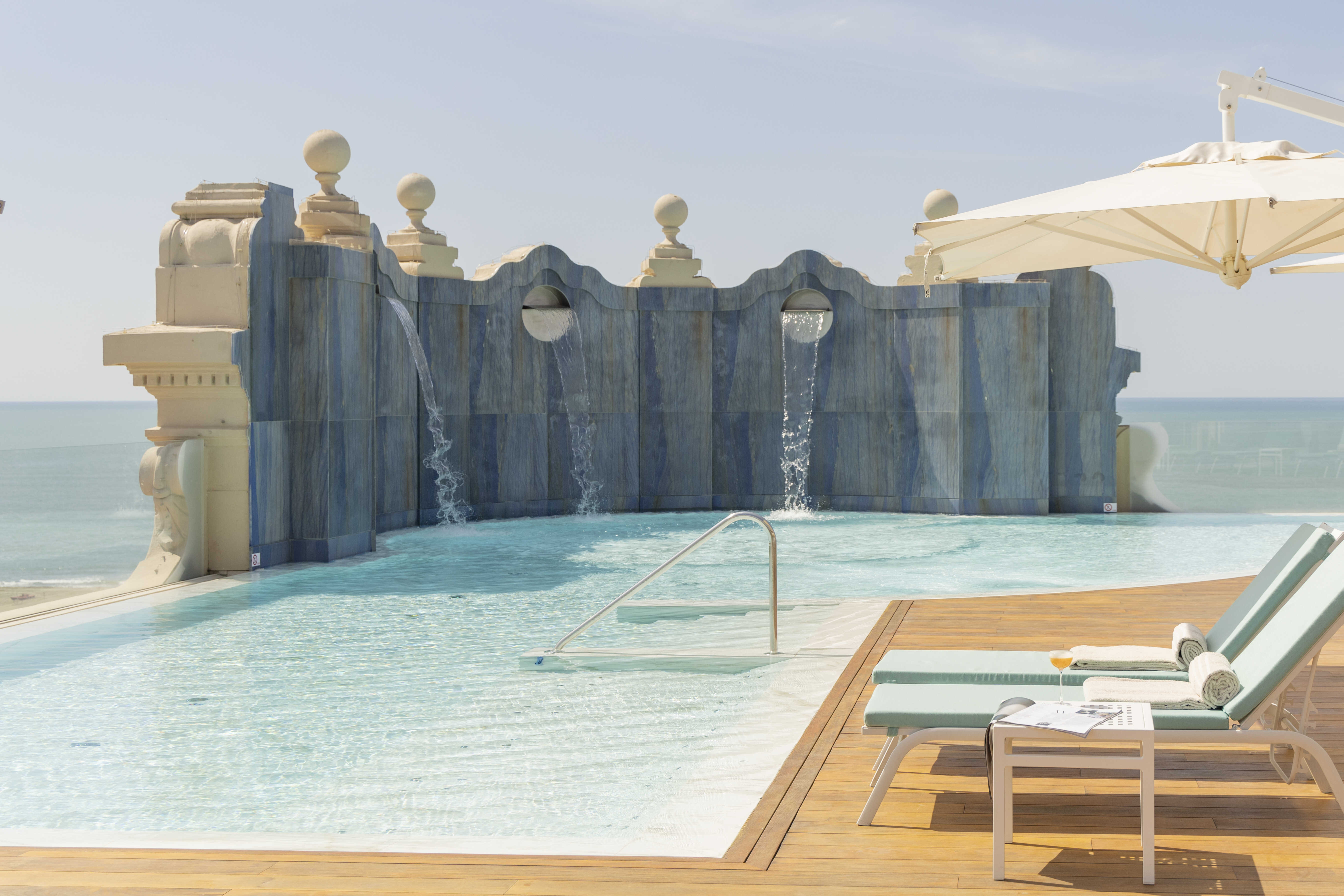 A rooftop pool with large stone wall and ocean views