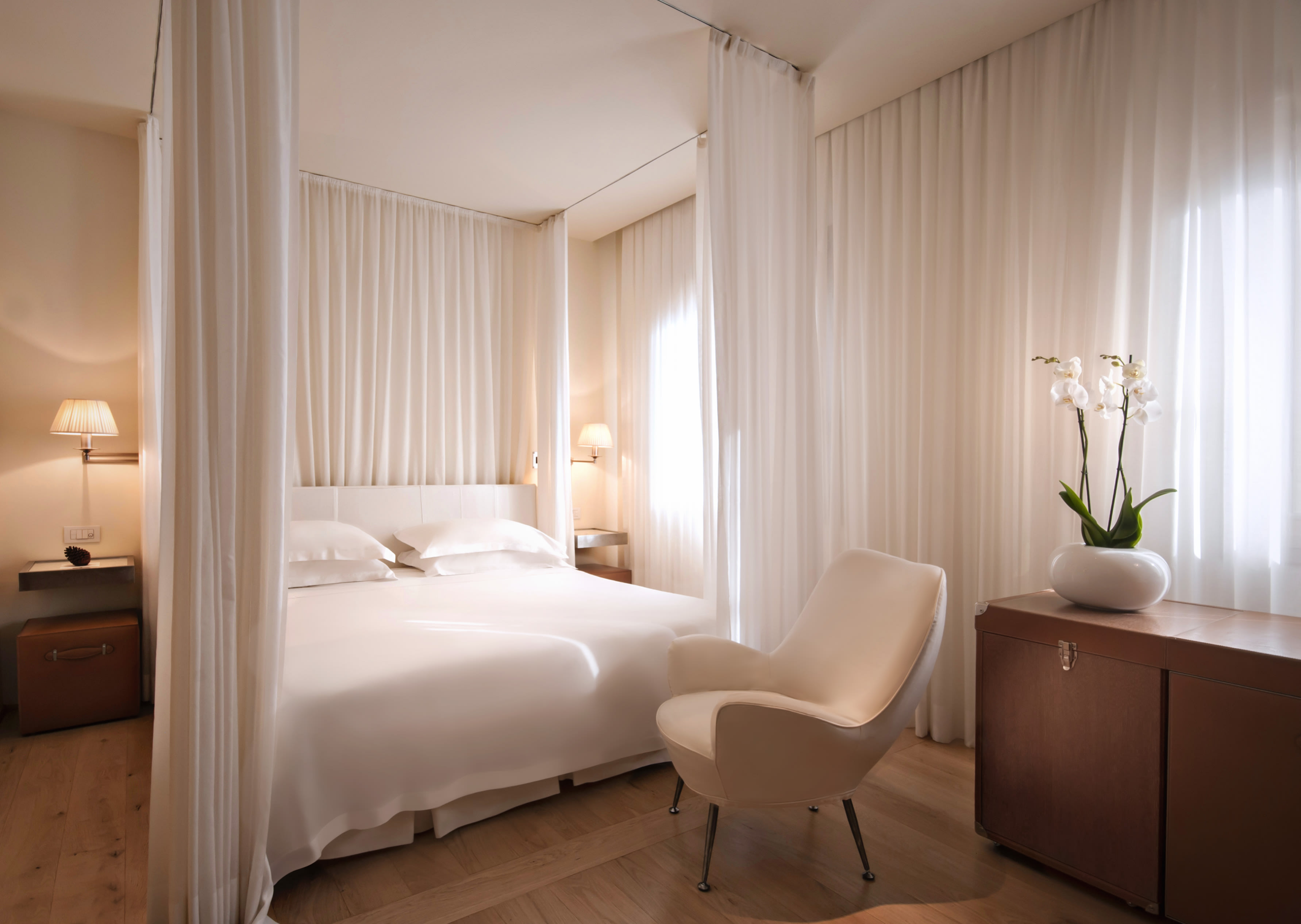 A hotel room with four-poster bed with white bedding and drapes