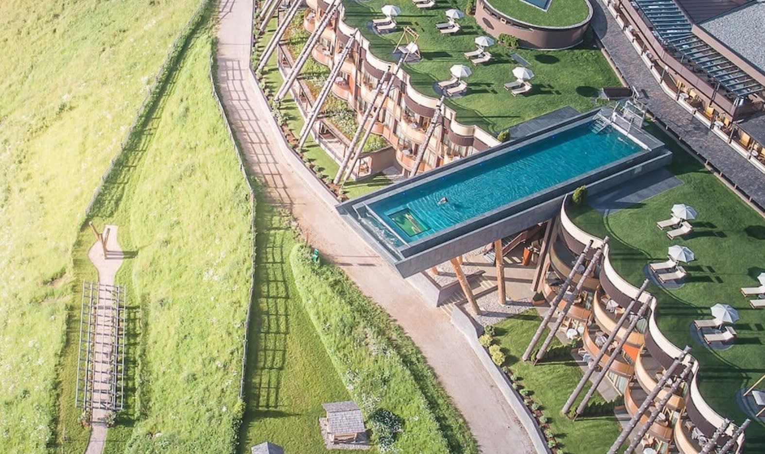 aerial view of pool extending over a green field below