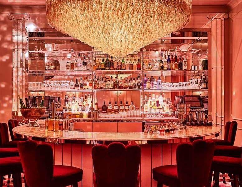 a swanky bar with velvet high chairs and pink lighting