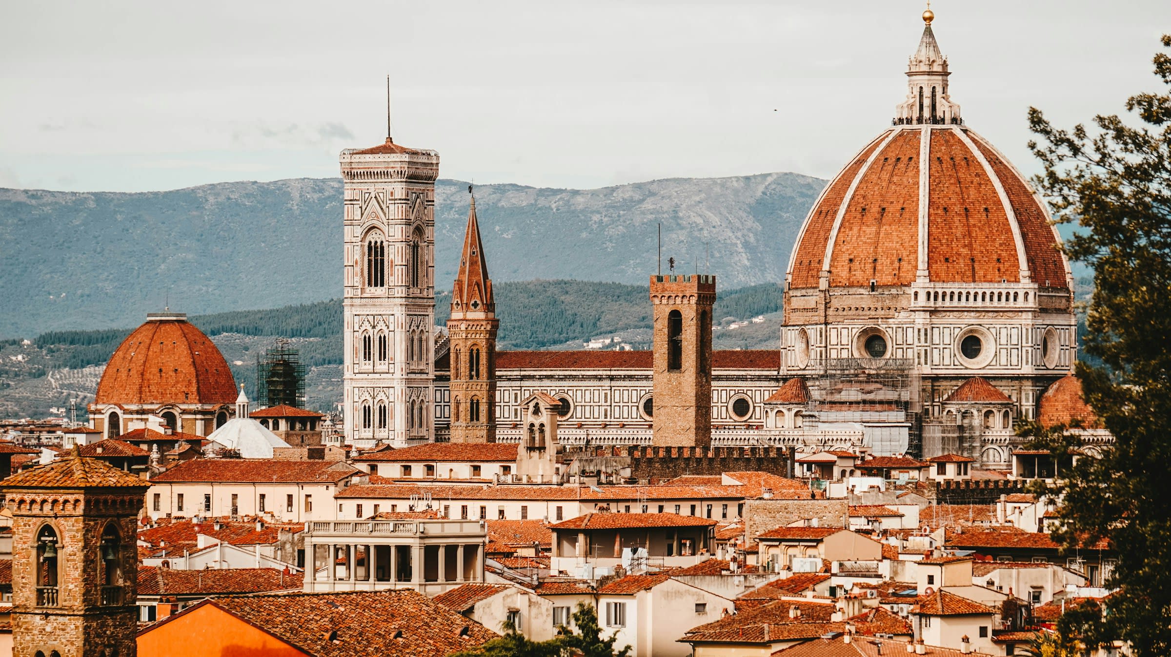 Brown domed building with tower and tan rooftops with hills in the background