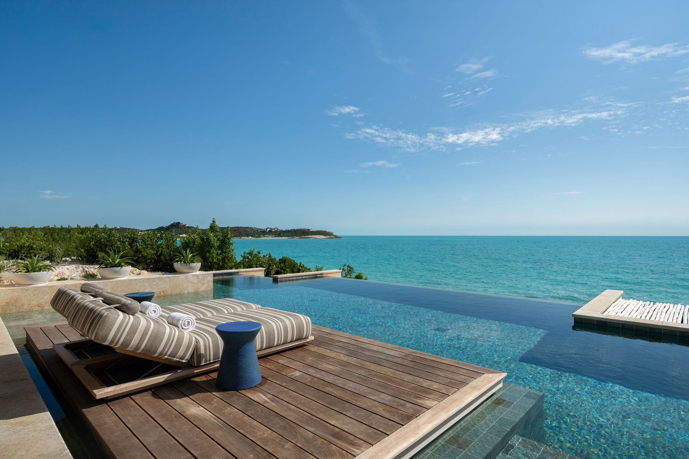 A hotel terrace with infinity pool and sun lounger overlooking turquoise ocean