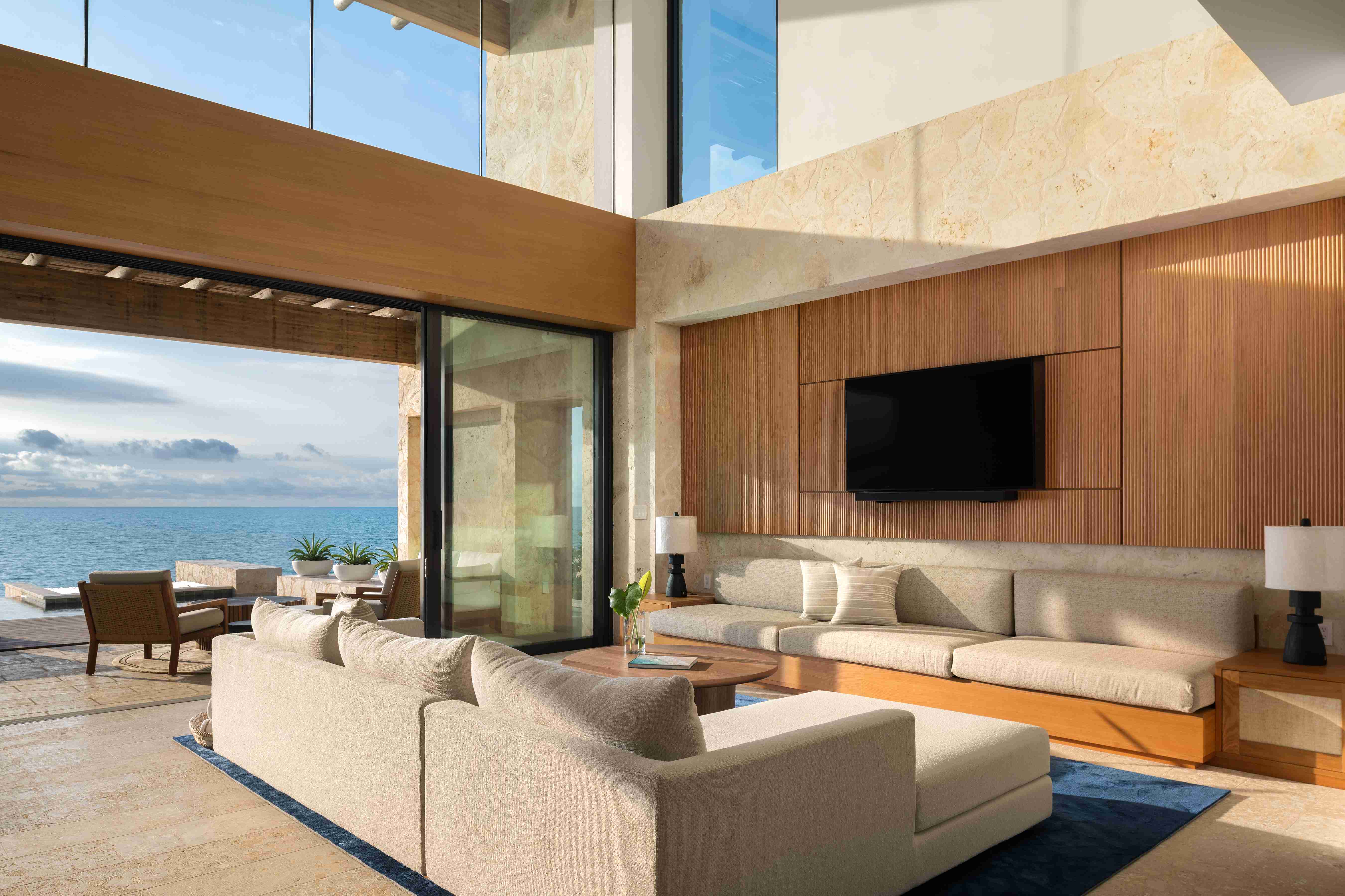 An upscale residence with double-height ceiling, neutral decor and furnishing and open floor-to-ceiling windows with ocean views