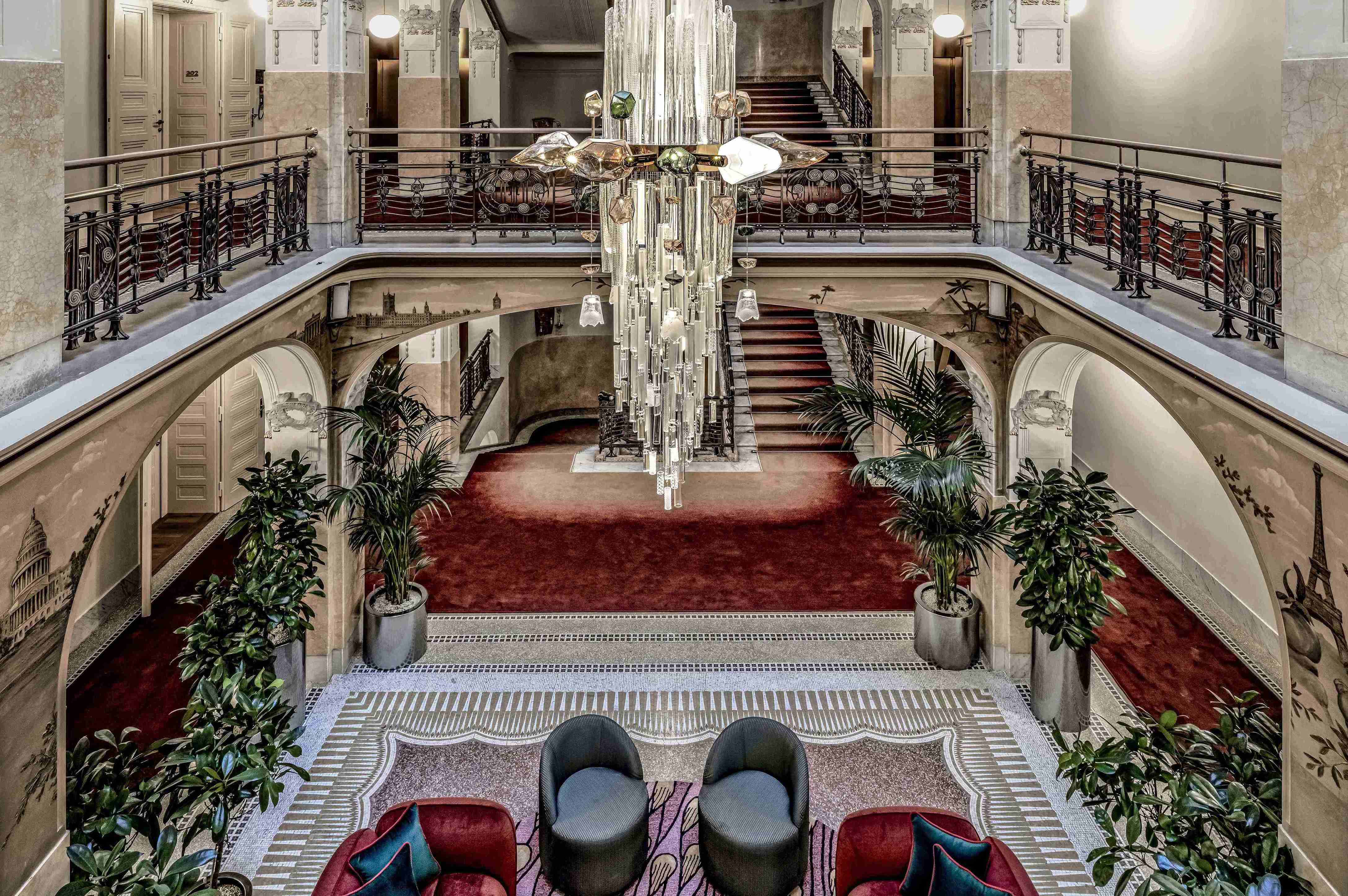 A grand hotel lobby with large chandelier and inner foyer with surrounding iron balconies and greenery