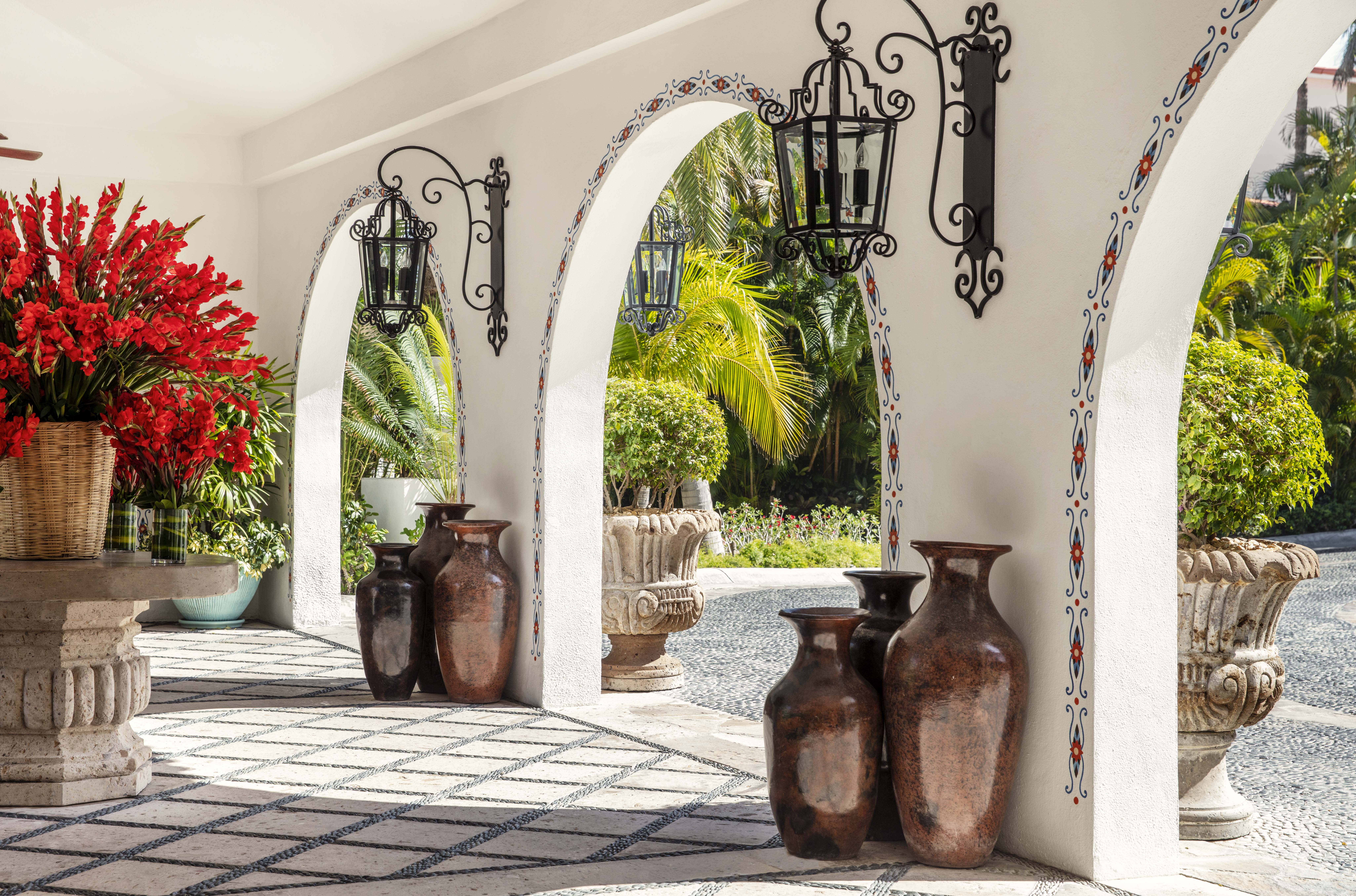A hotel lobby area with white archways, bright flowers, and antique standing vases