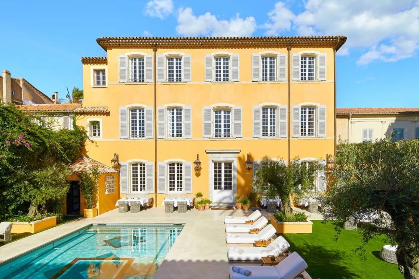 yellow villa with a pool and white shutters with a blue sky