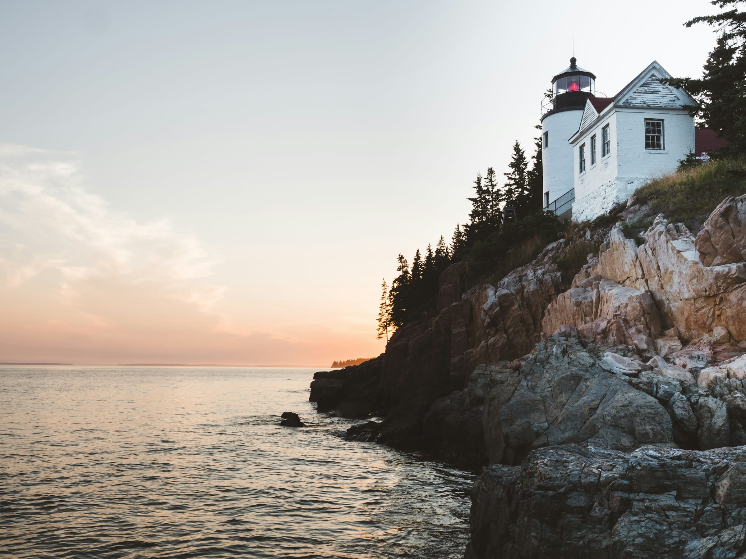 white lighthouse on top of a rocky outcrop near the sea at dusk