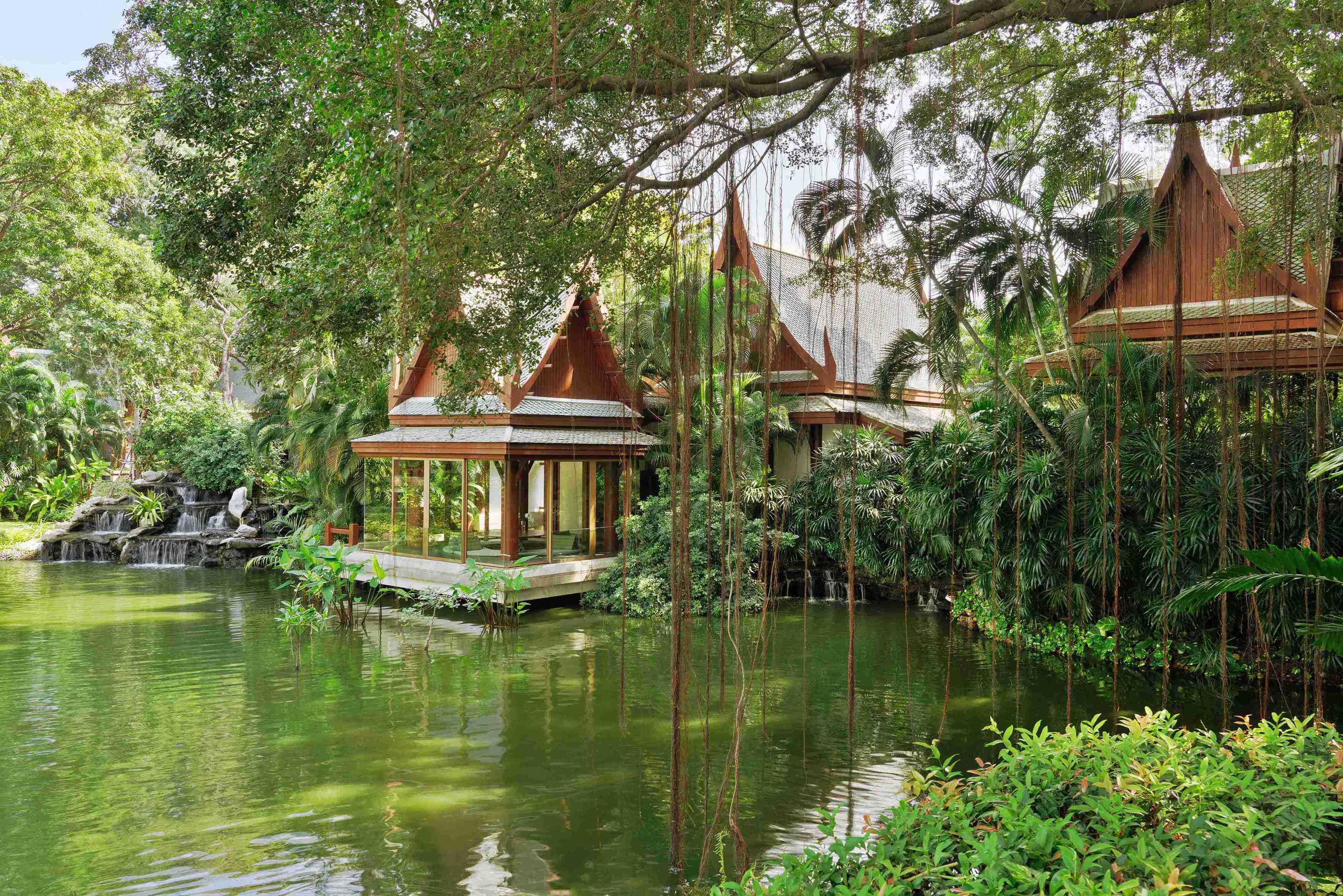 A serene lake with verdant foliage all around and traditional Thai structures
