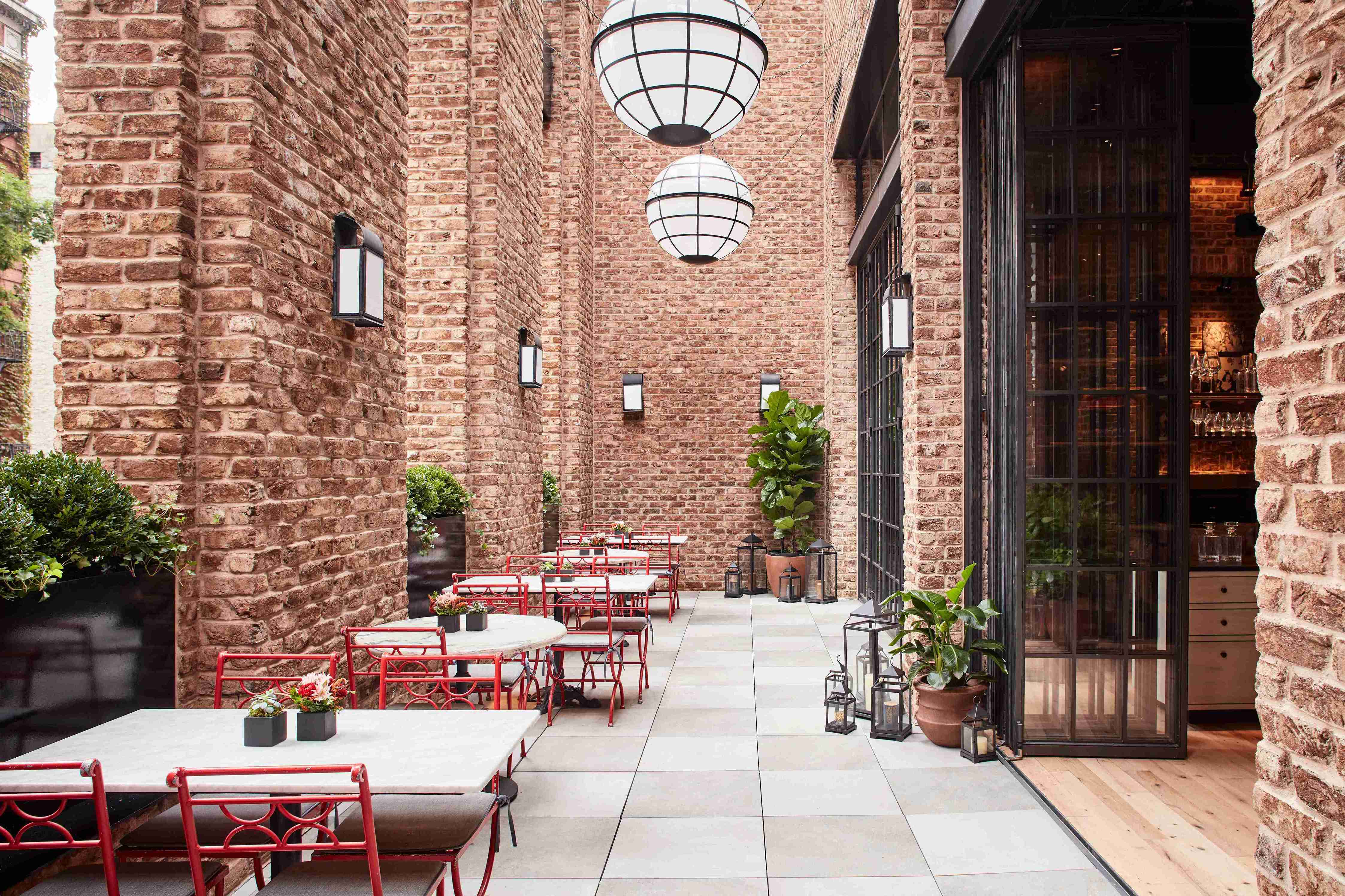 An outdoor terrace with high brick walls and hanging lamps with dark iron doors