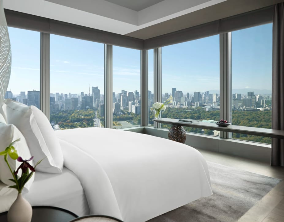 A modern corner suite with floor-to-ceiling windows overlooking Tokyo’s skyline and a city park.