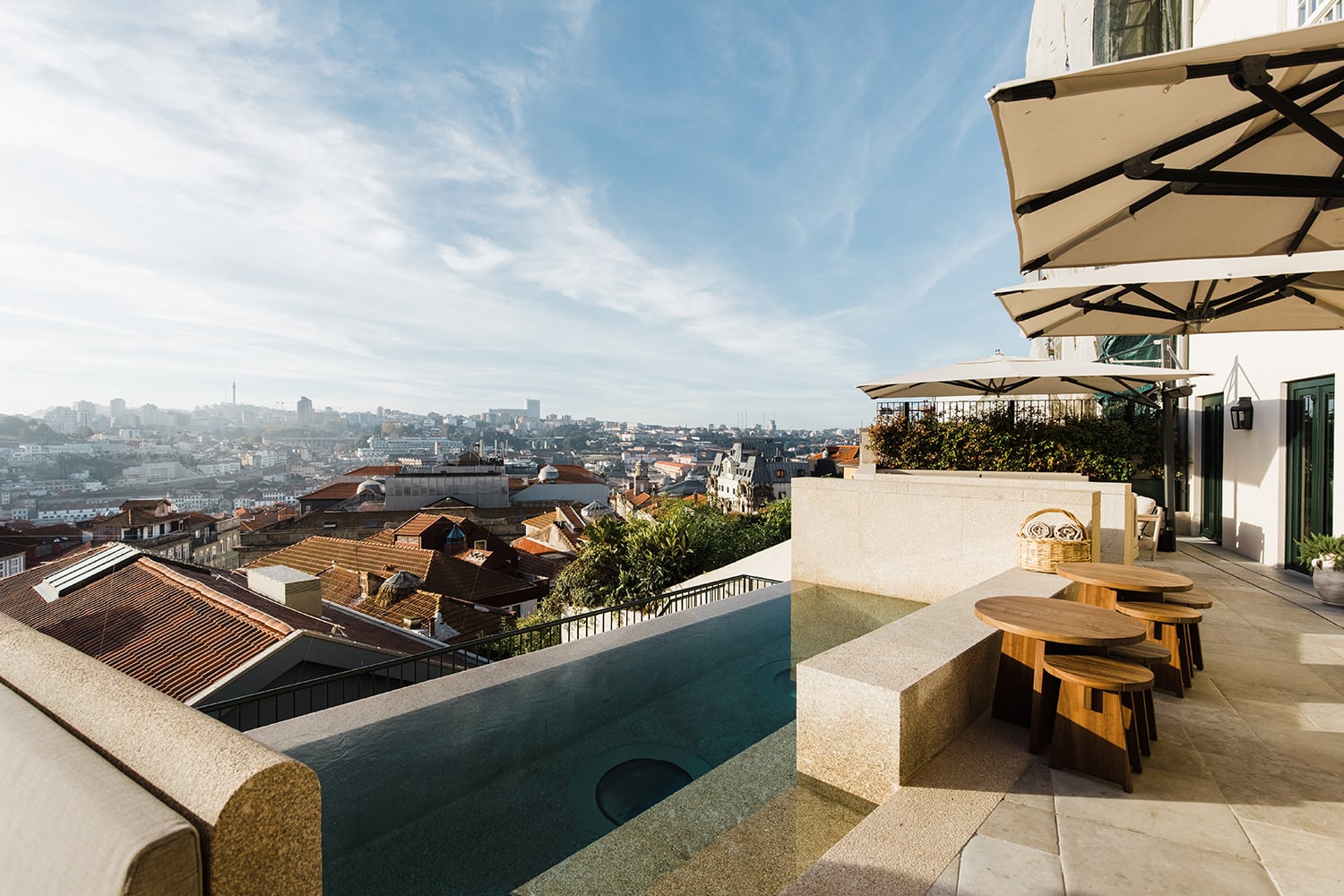 small rooftop pool with umbrellas and seating overlooking a city with blue skies