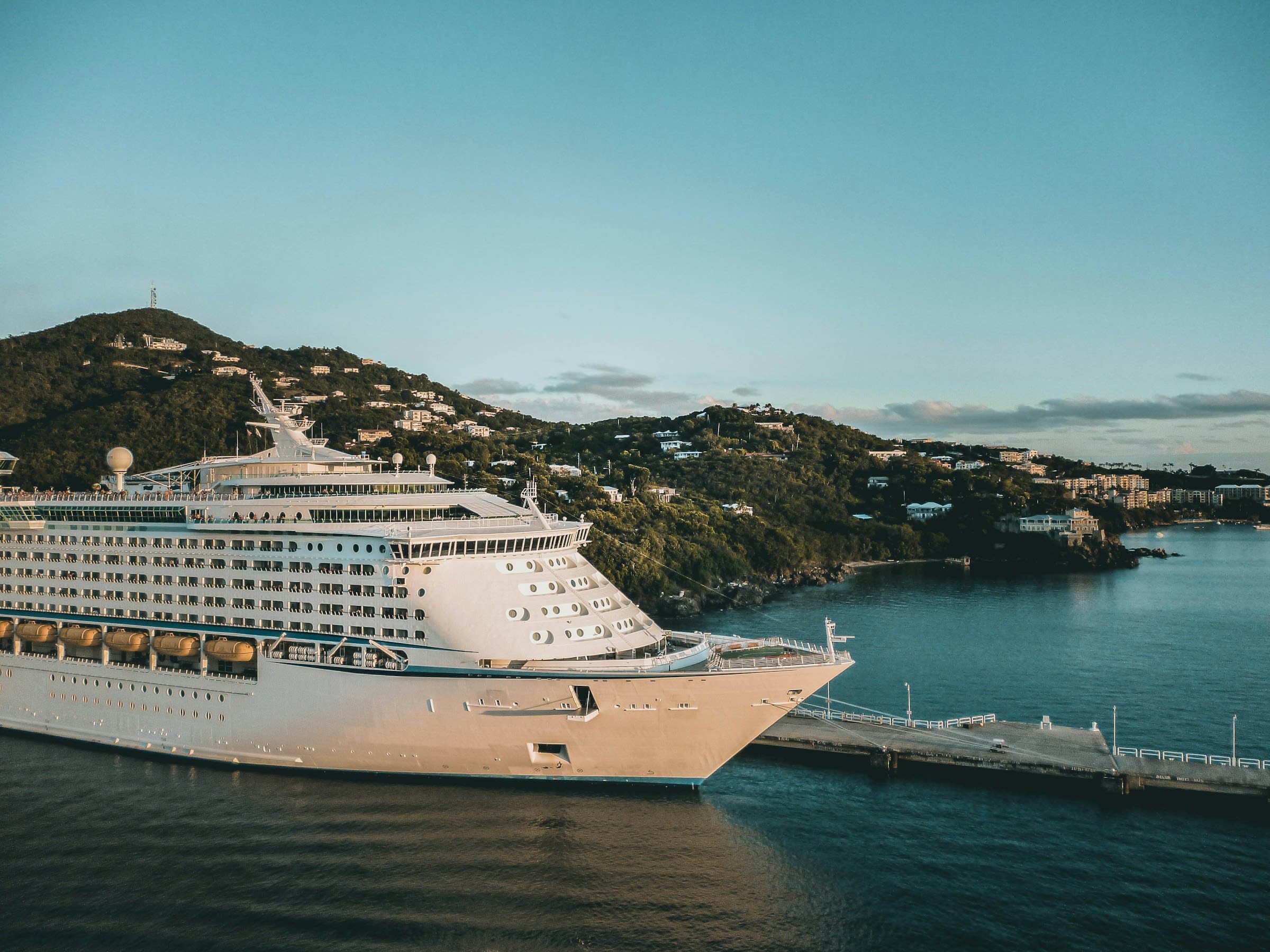 white cruise ship in port with homes dotting the green hills during daytime