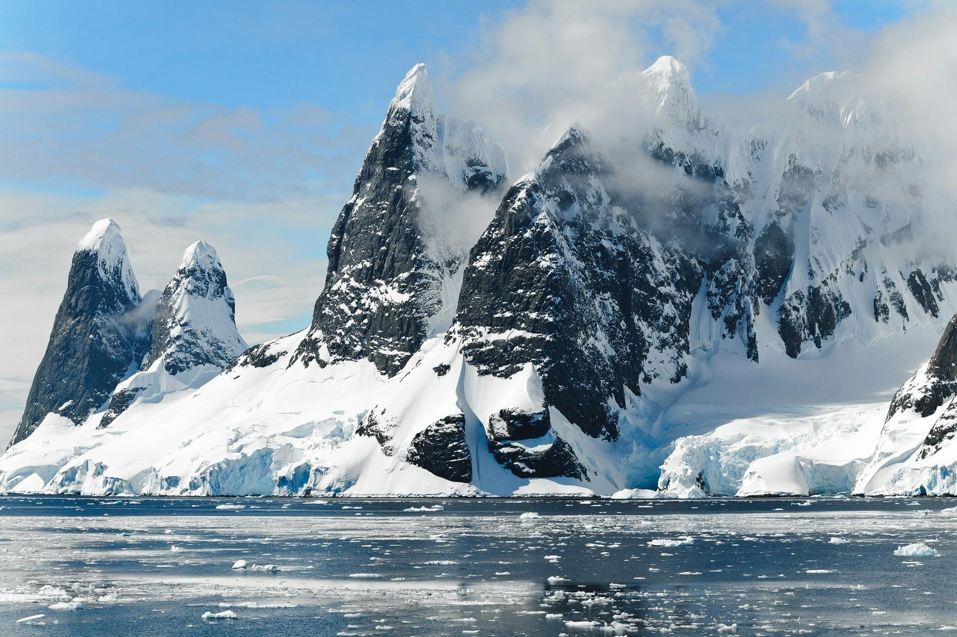Black rock mountains covered in snow with icy ocean waters beside it during day