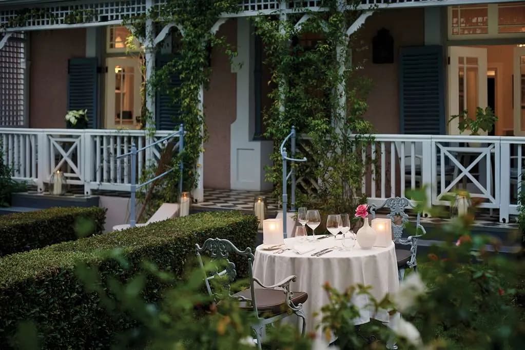 A white-tablecloth-clad table in a garden in front of a villa