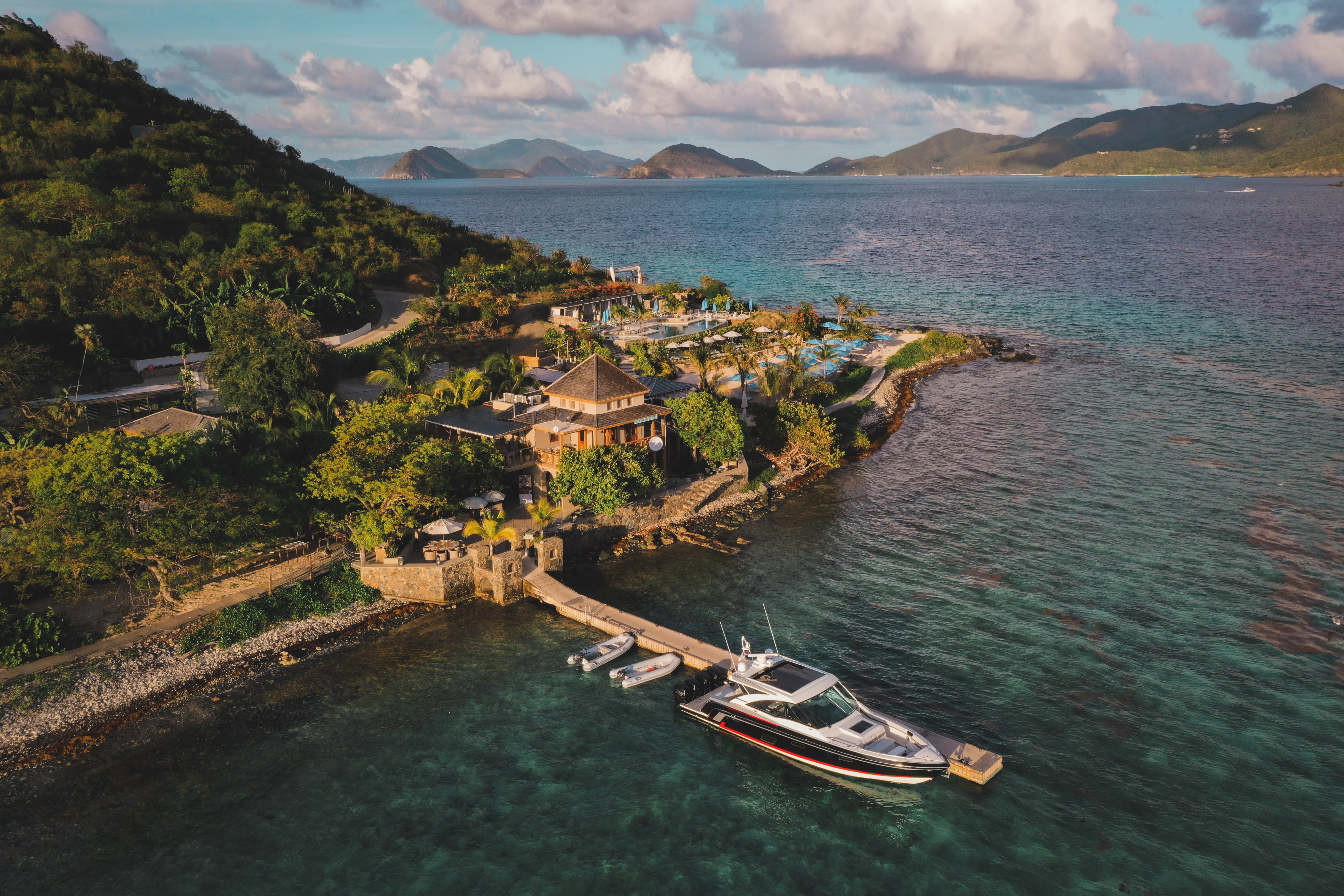 A private pier on a tropical island with a yacht docked and low-rise buildings and lush foliage surrounding