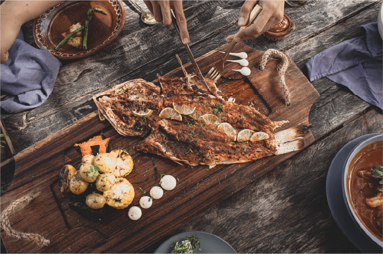 A whole fish in marinade on a large wooden board, served with potatoes and garnish