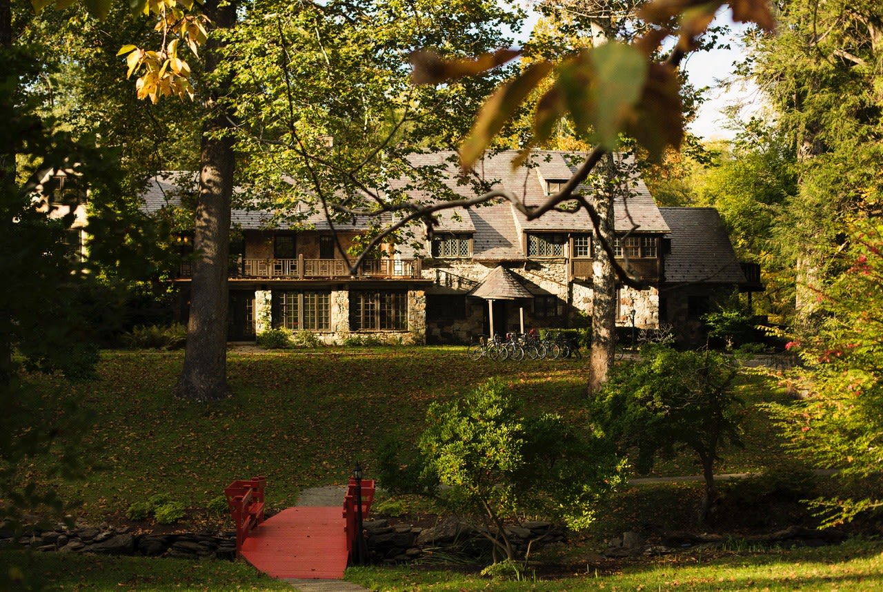 Charming stone lodge nestled in a forested setting with a red footbridge and bicycles out front, surrounded by autumn foliage.