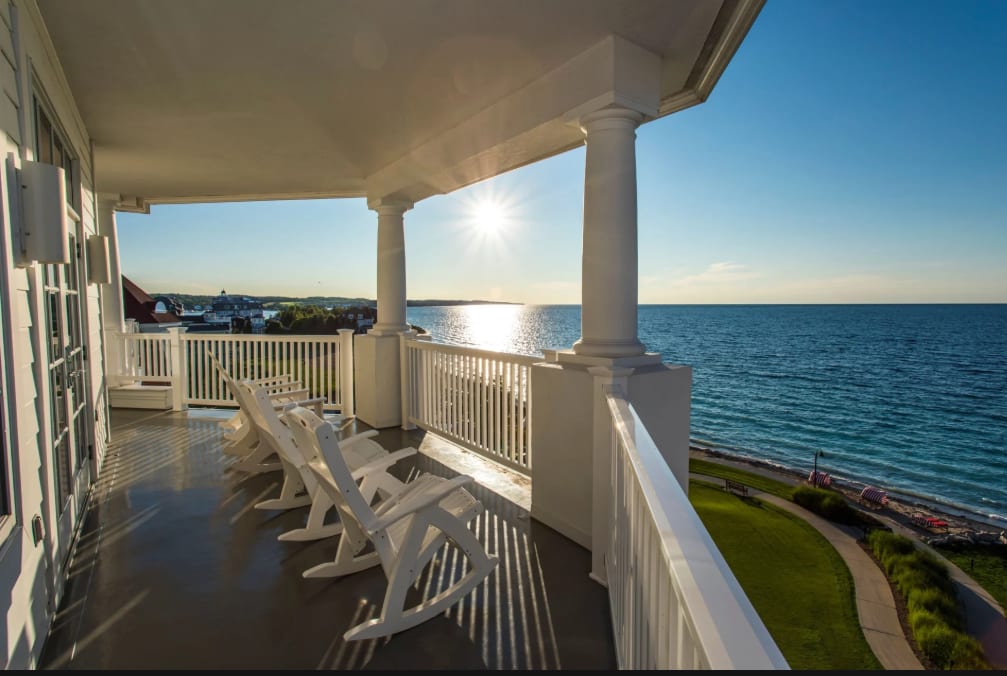 A balcony with white picket fence and deck chairs looking out at the ocean with the sun low in the sky.