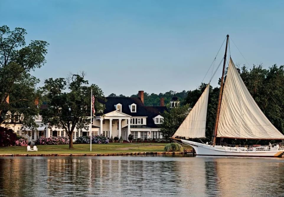 A large sailboat docked on a lake outside an elegant white building.