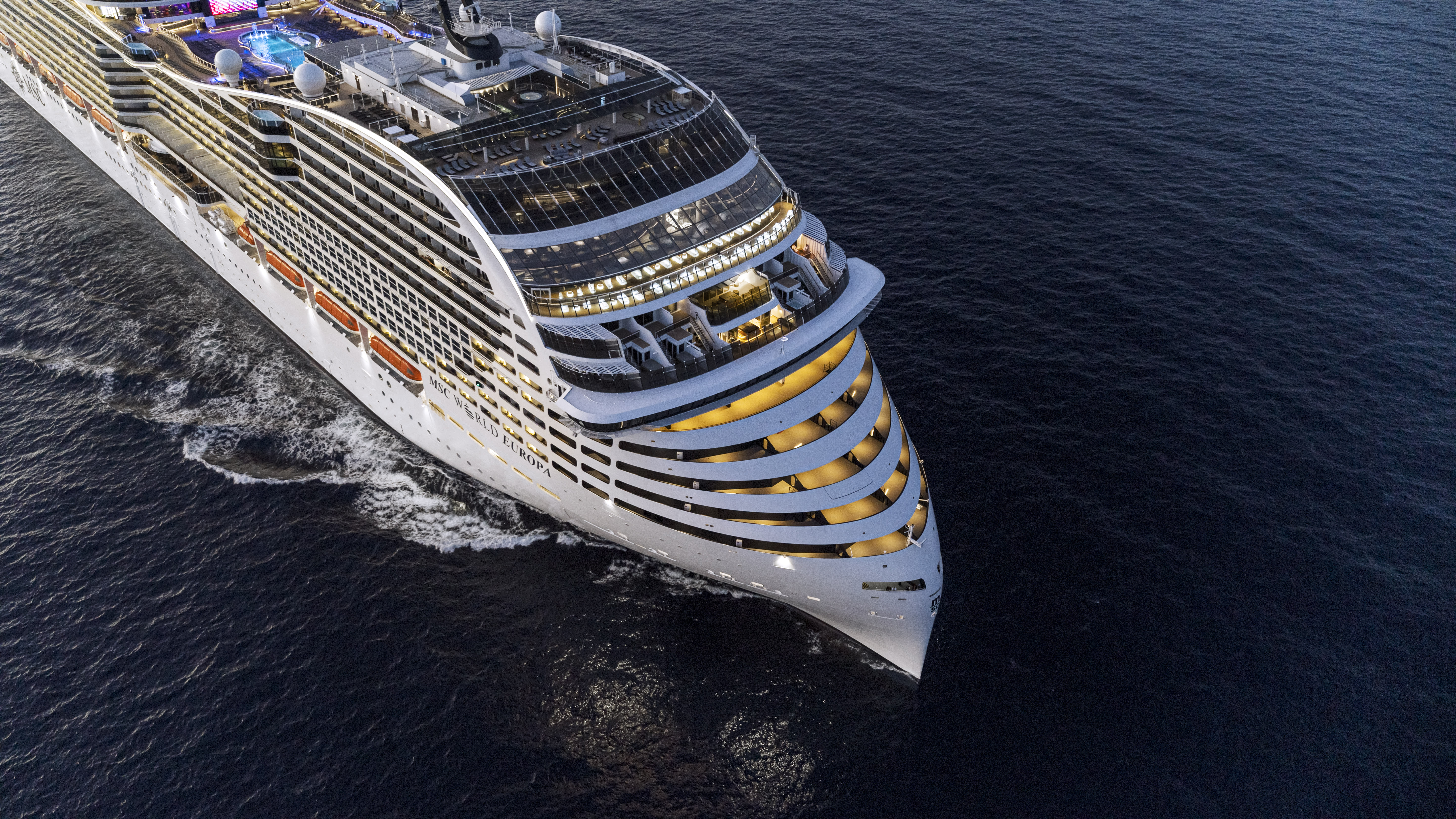 Aerial shot of the front of a sleek, futuristic looking cruise ship in the ocean at dusk