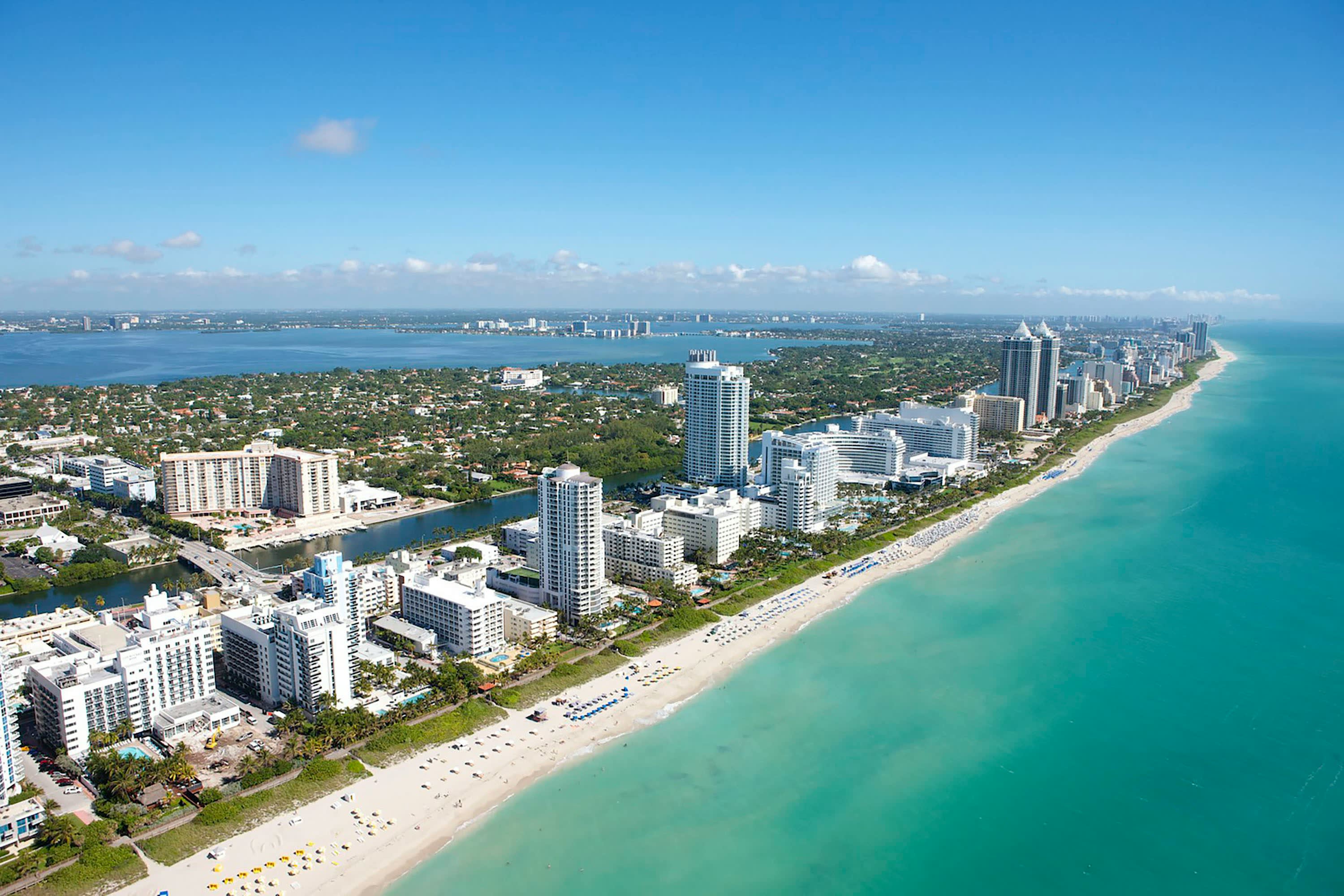 aerial view of beachfront buildings with turquoise ocean waters and large city behind