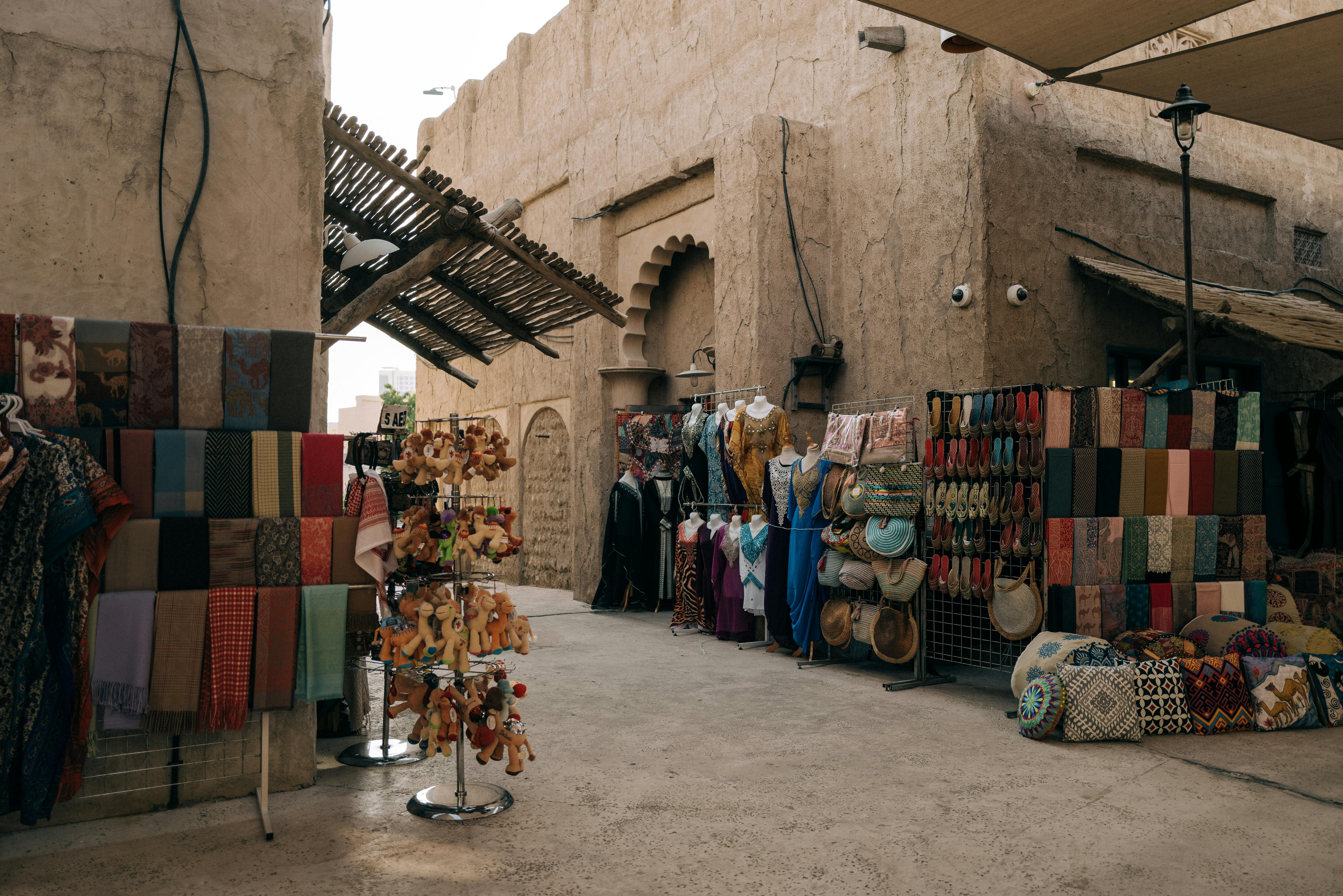 variety of colorful souvenirs on display in a middle eastern souk with tan buildings and dirt floor
