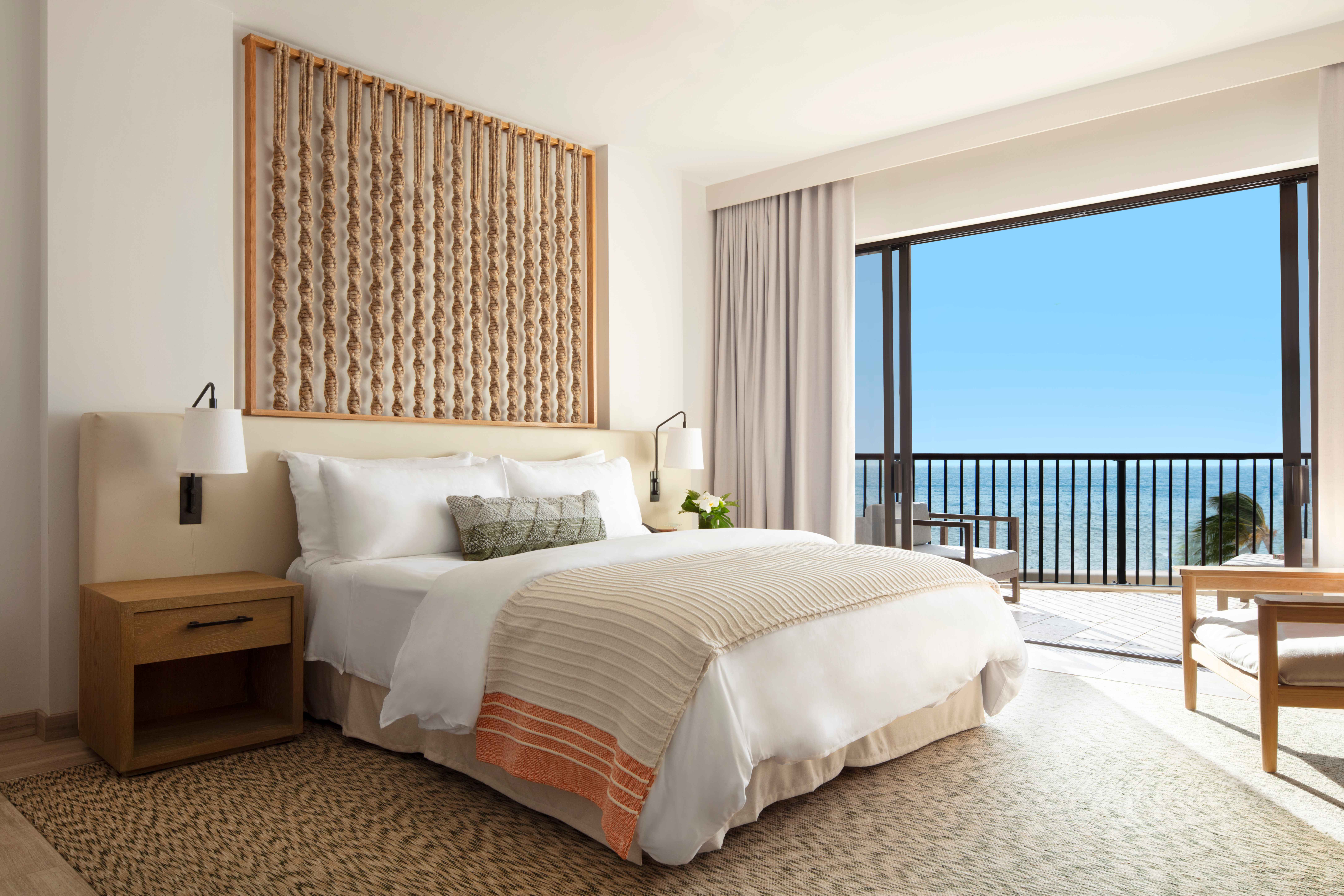 An elegant hotel room with cream and neutral furnishing and decor, with ocean views.