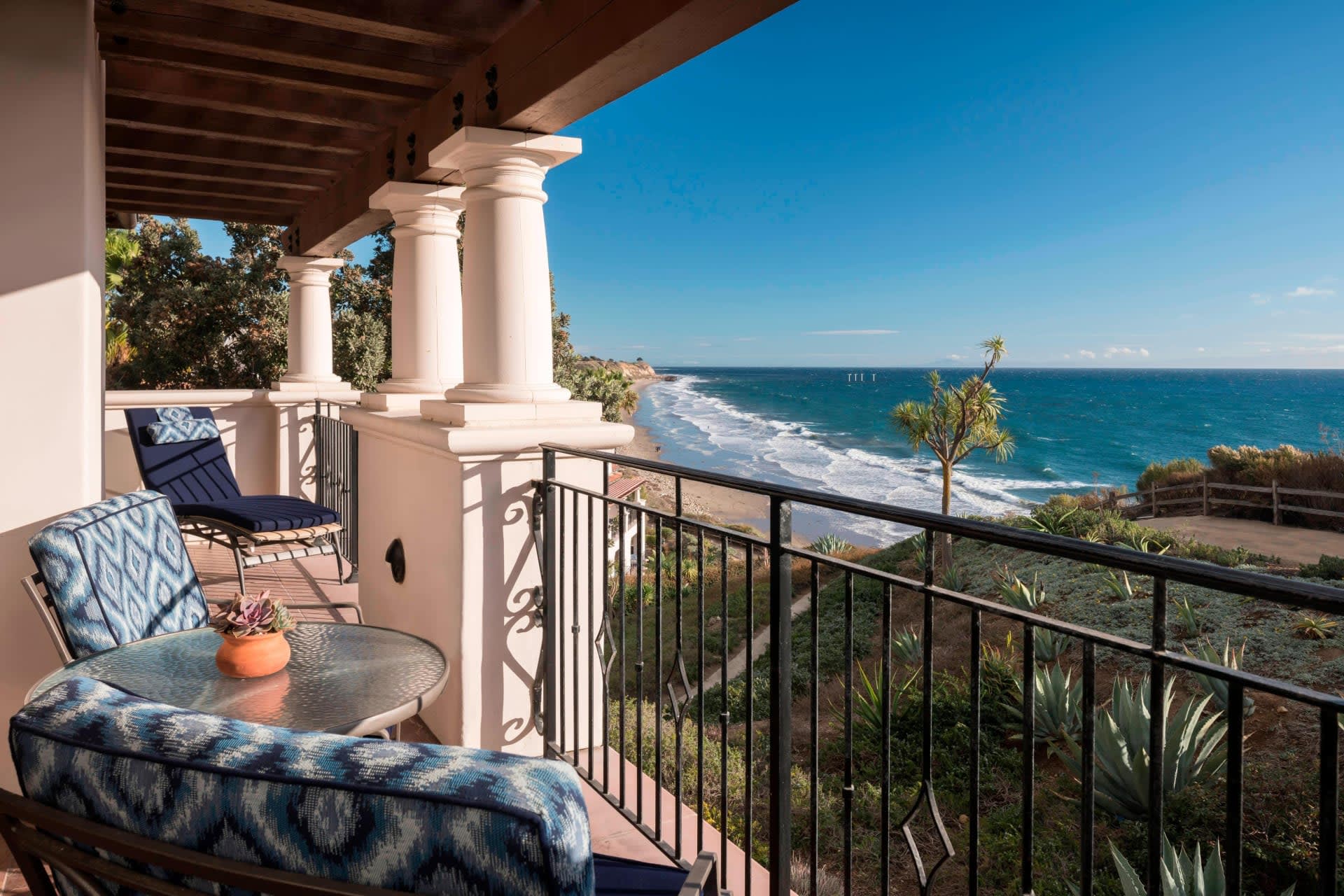 A balcony with two chairs, cast iron railing, a small table and ocean views.