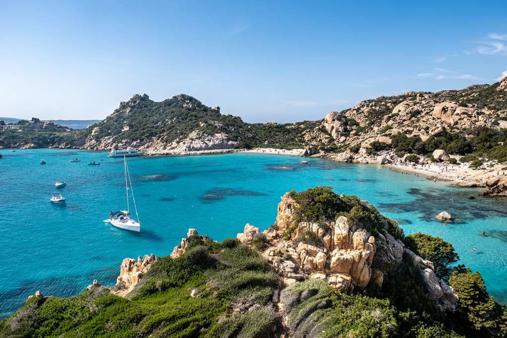 Turquoise water cove with boats, and grass covered rocky hills surrounding the bay in daytime