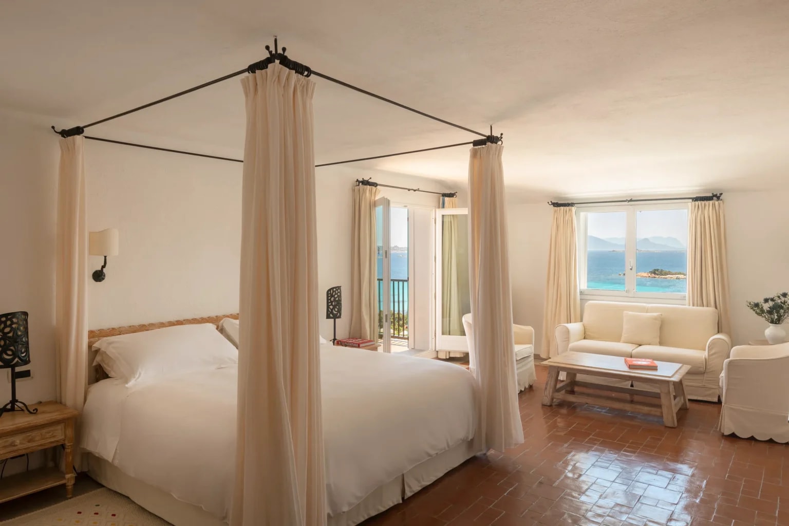 A white hotel room with white curtain four poster bed, and white couch