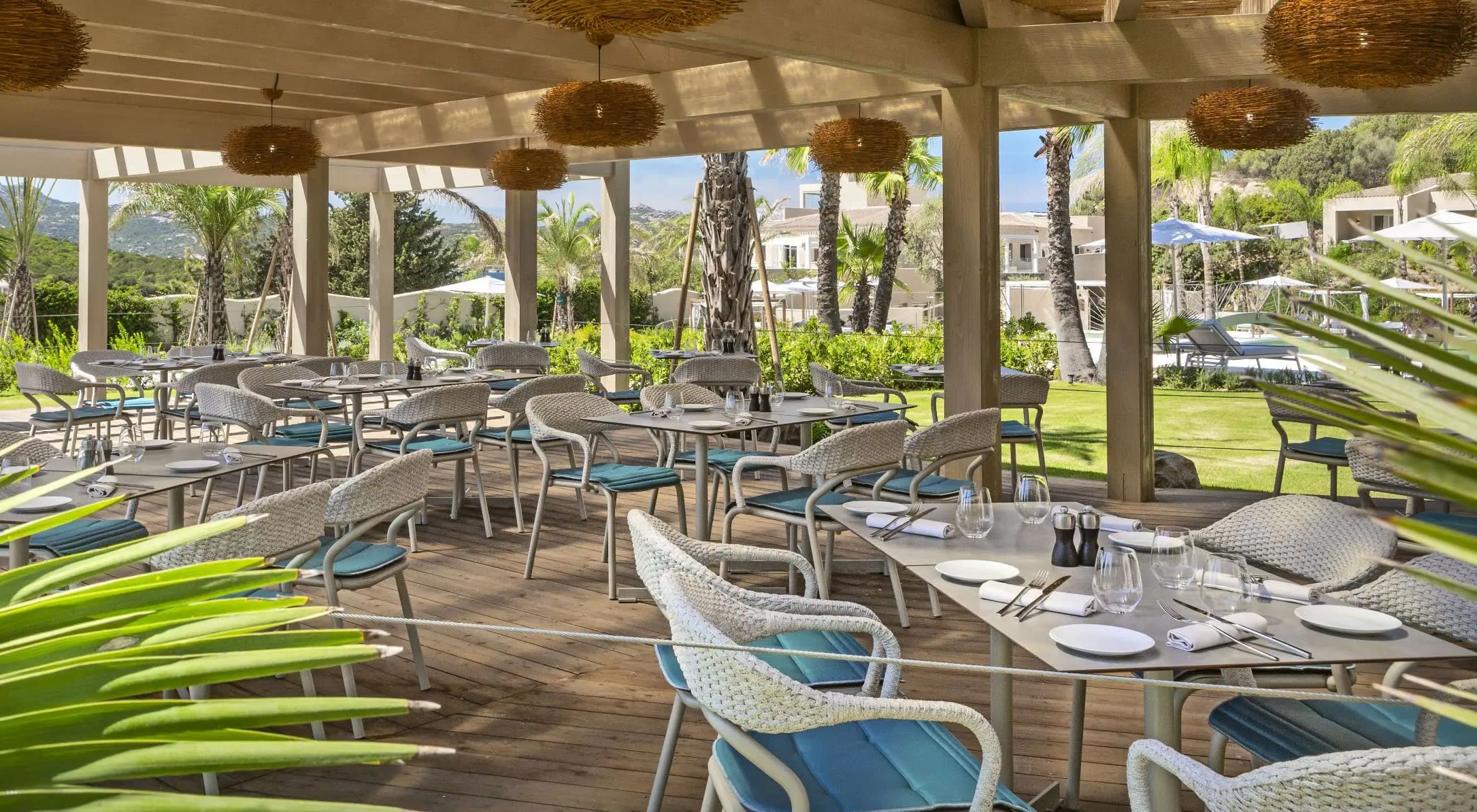 An outdoor dining patio with white furniture and blue cushions, plus tropical trees and wood roof