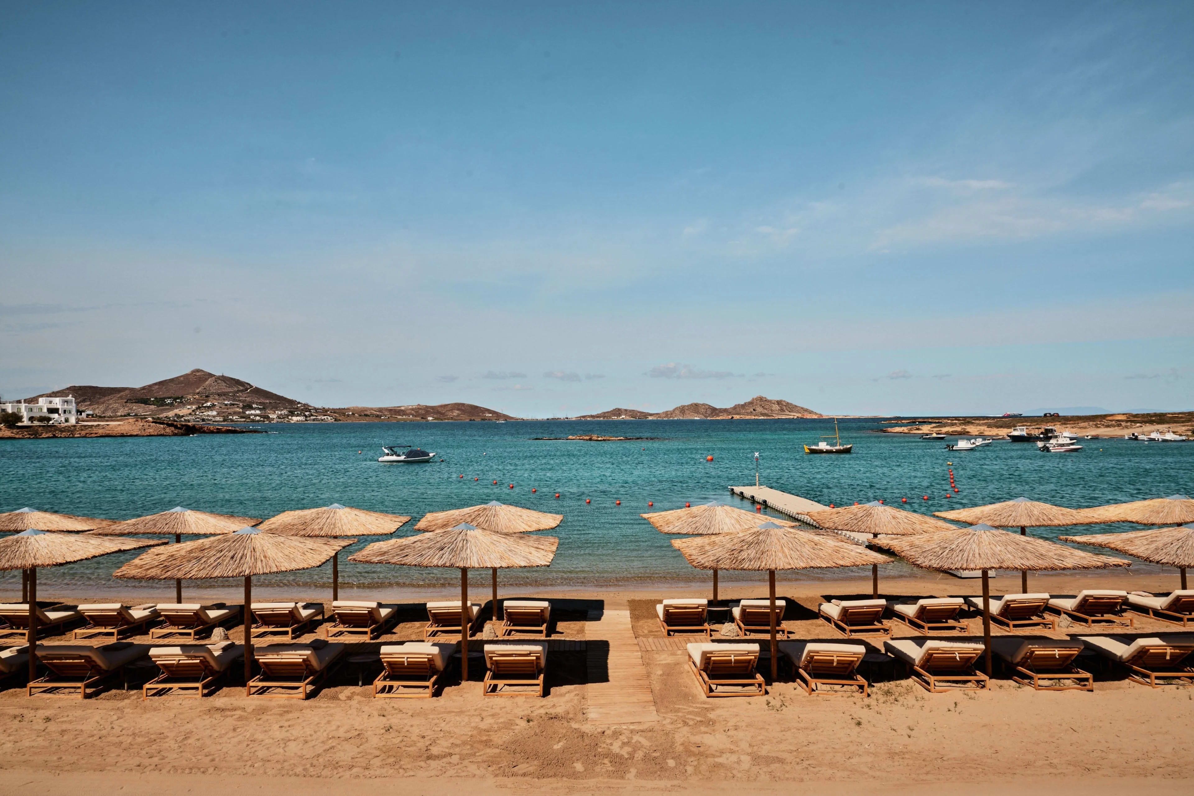 beach club with brown lounge chairs and wood umbrellas on a beach with turquoise water during day