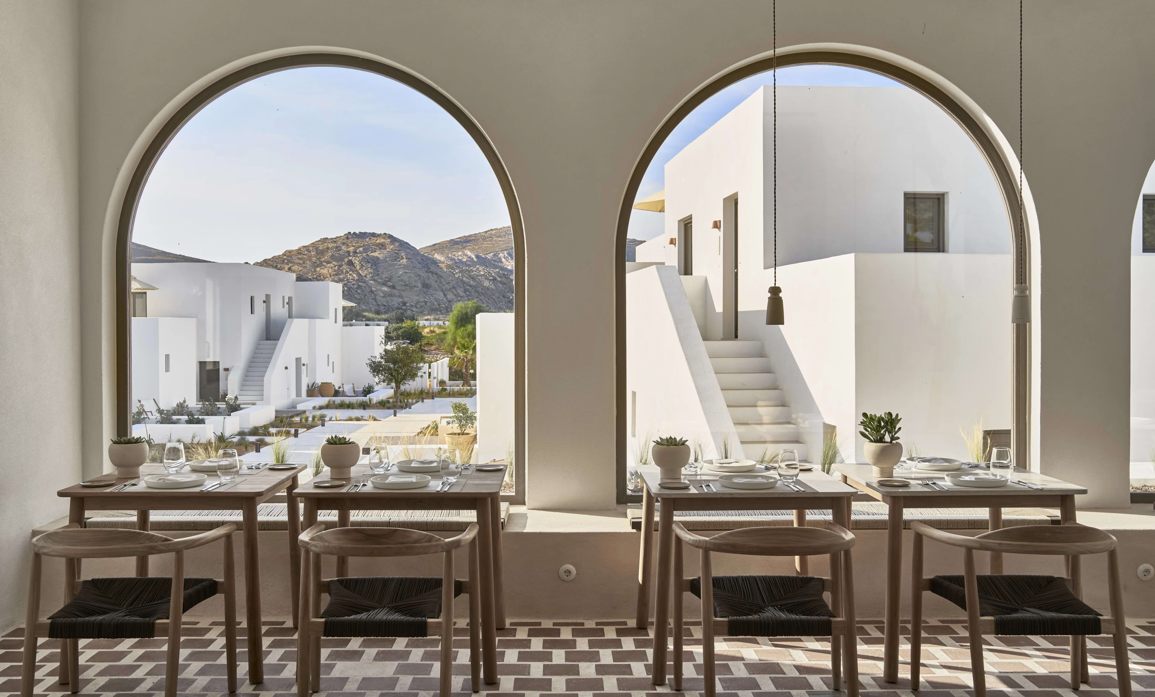 inside of a restaurant with tables and chairs under two giant windows with white buildings and mountains outside during day