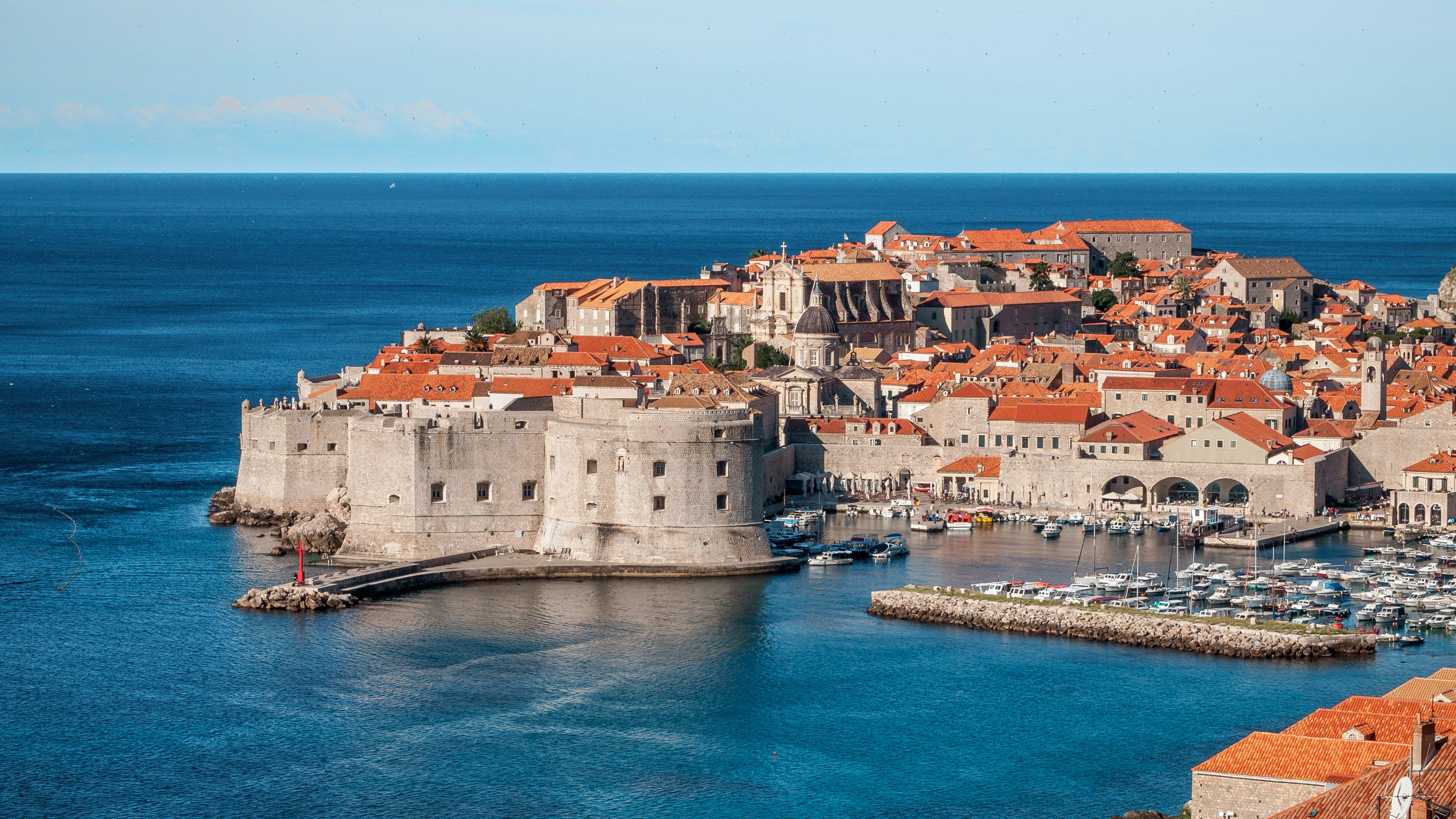 a walled, fortified old city with red roofs and harbor next to turquoise ocean water during day