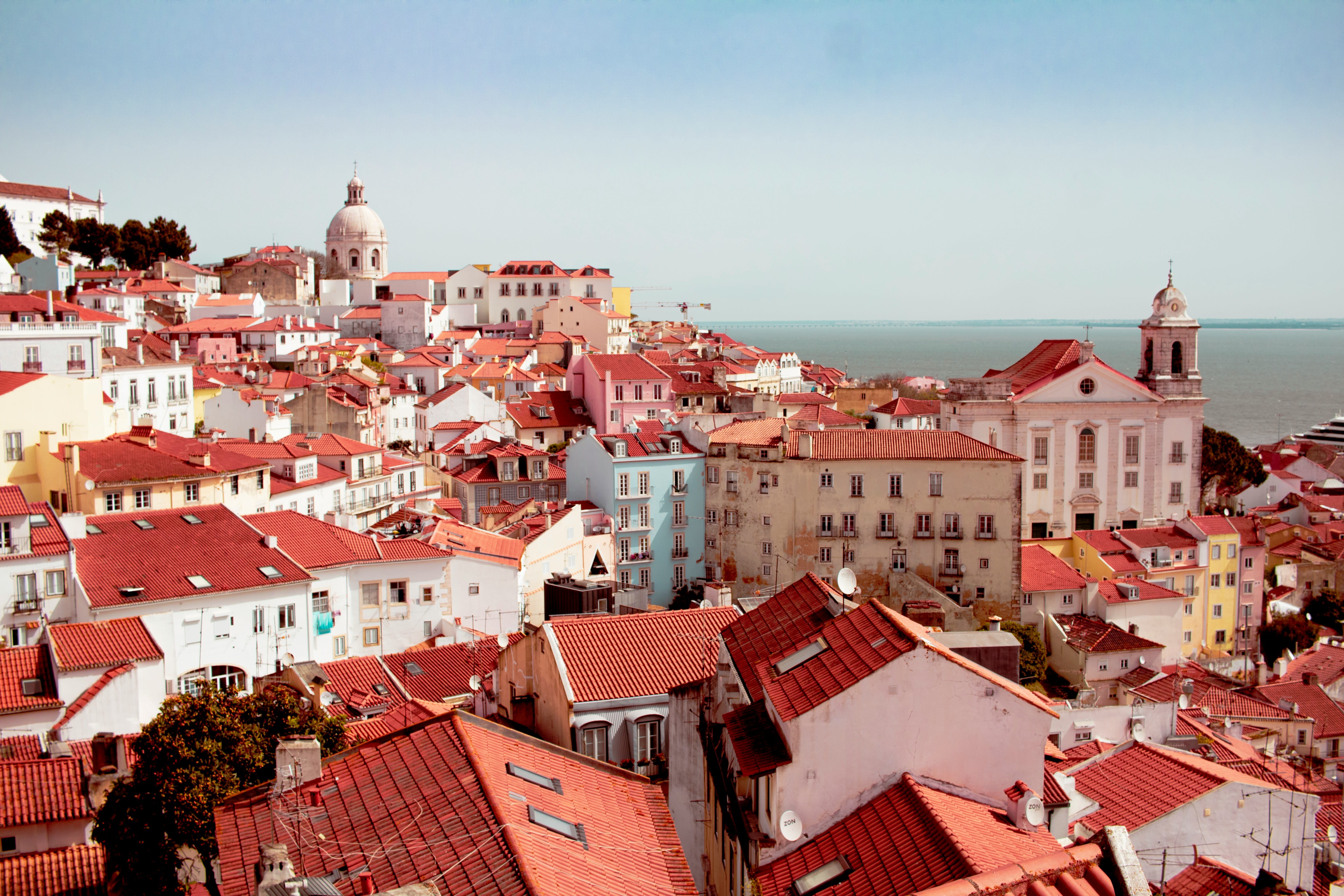 Colorful red-roofed buildings in Lisbon’s historic Alfama district under a clear blue sky by the river.