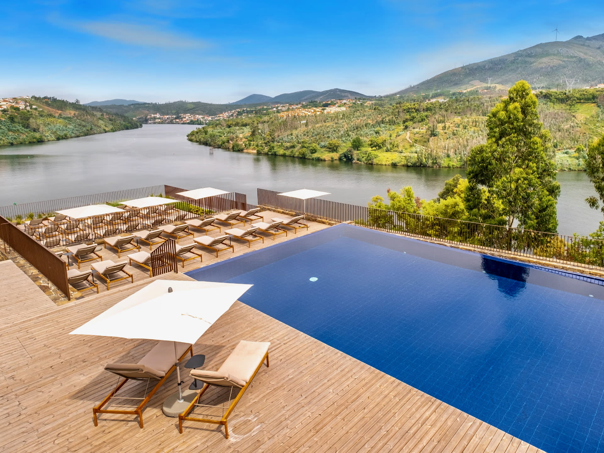 Pool and wood deck eith chaise lounges overlooking a river valley during day