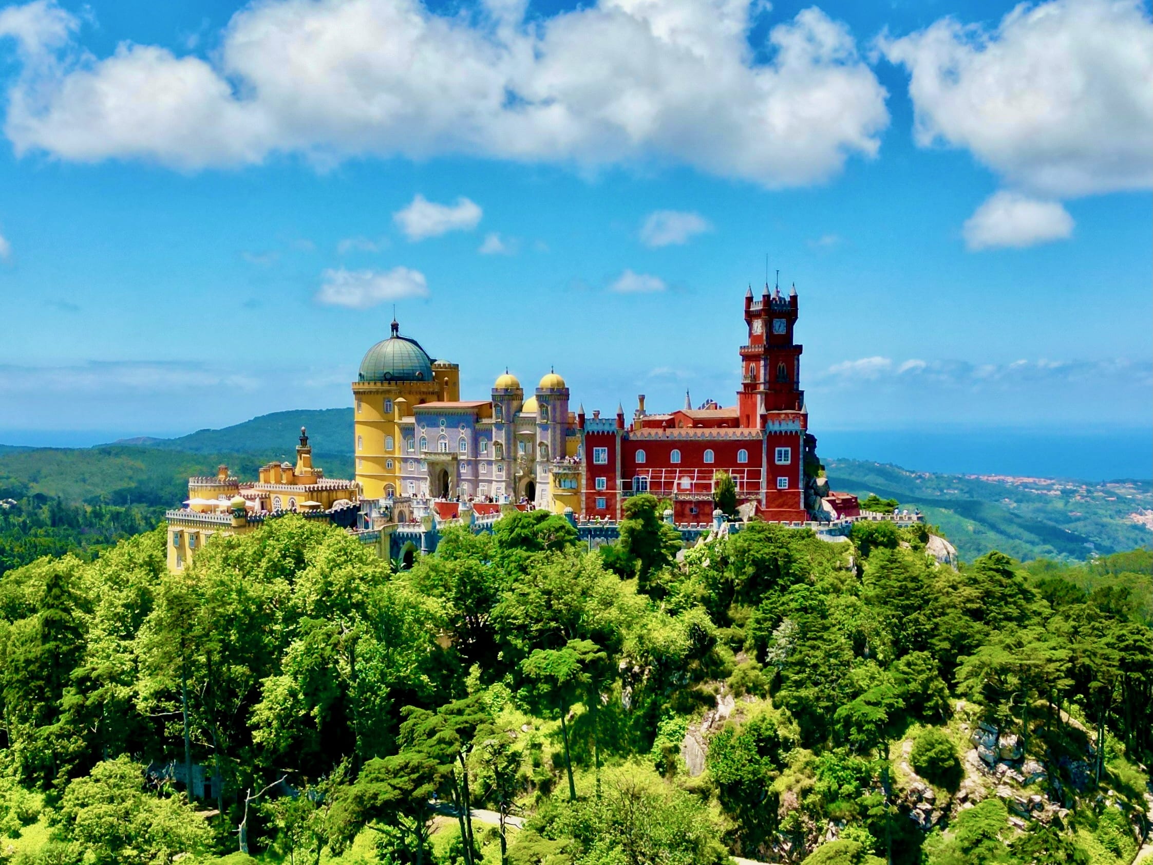 a colorful yellow and red castle on top of a vibrant green hill during day