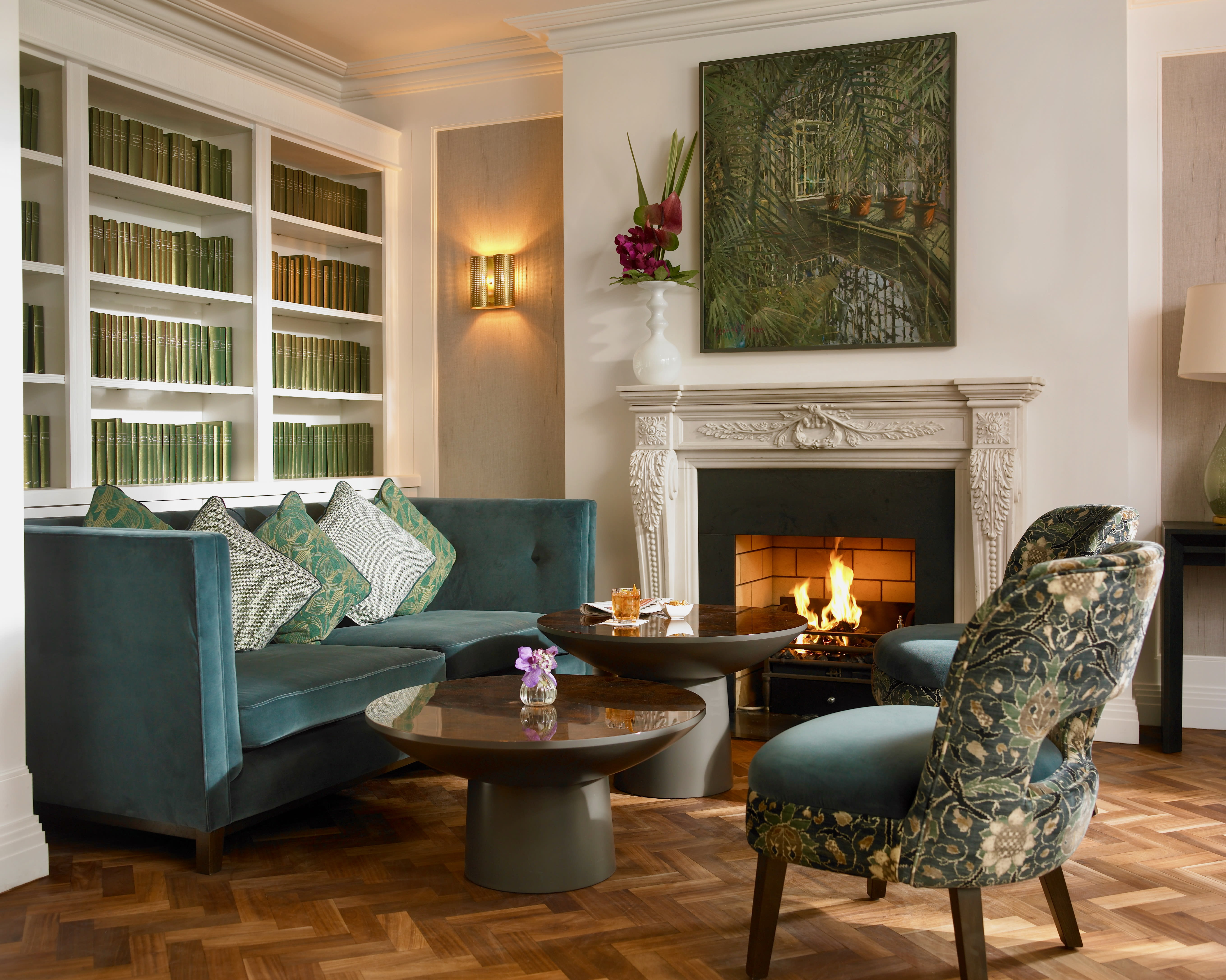 cozy library with green books, green painting above a lit white fireplace and green seating