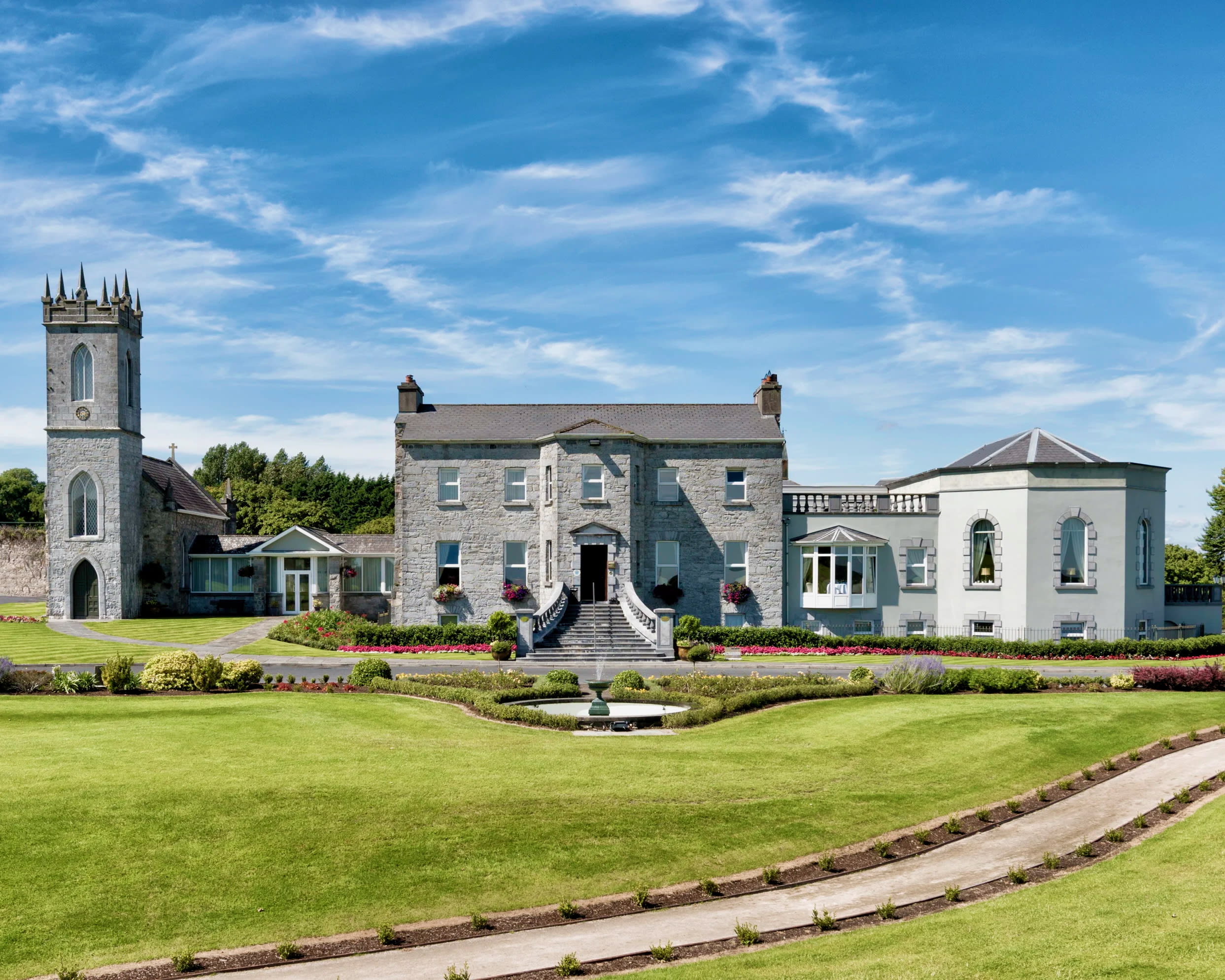 A grey stone building with tower, green grass and bright blue sky