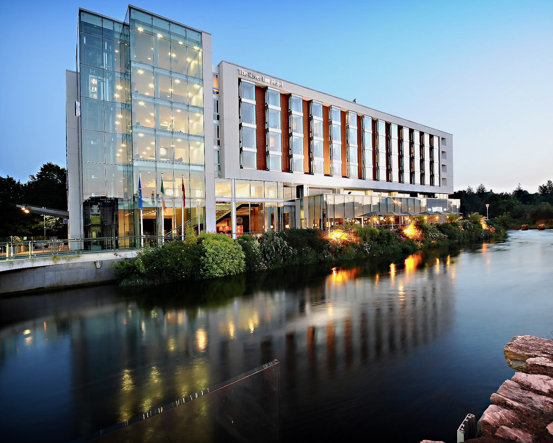 a modern building with white walls and glass on a river at dusk
