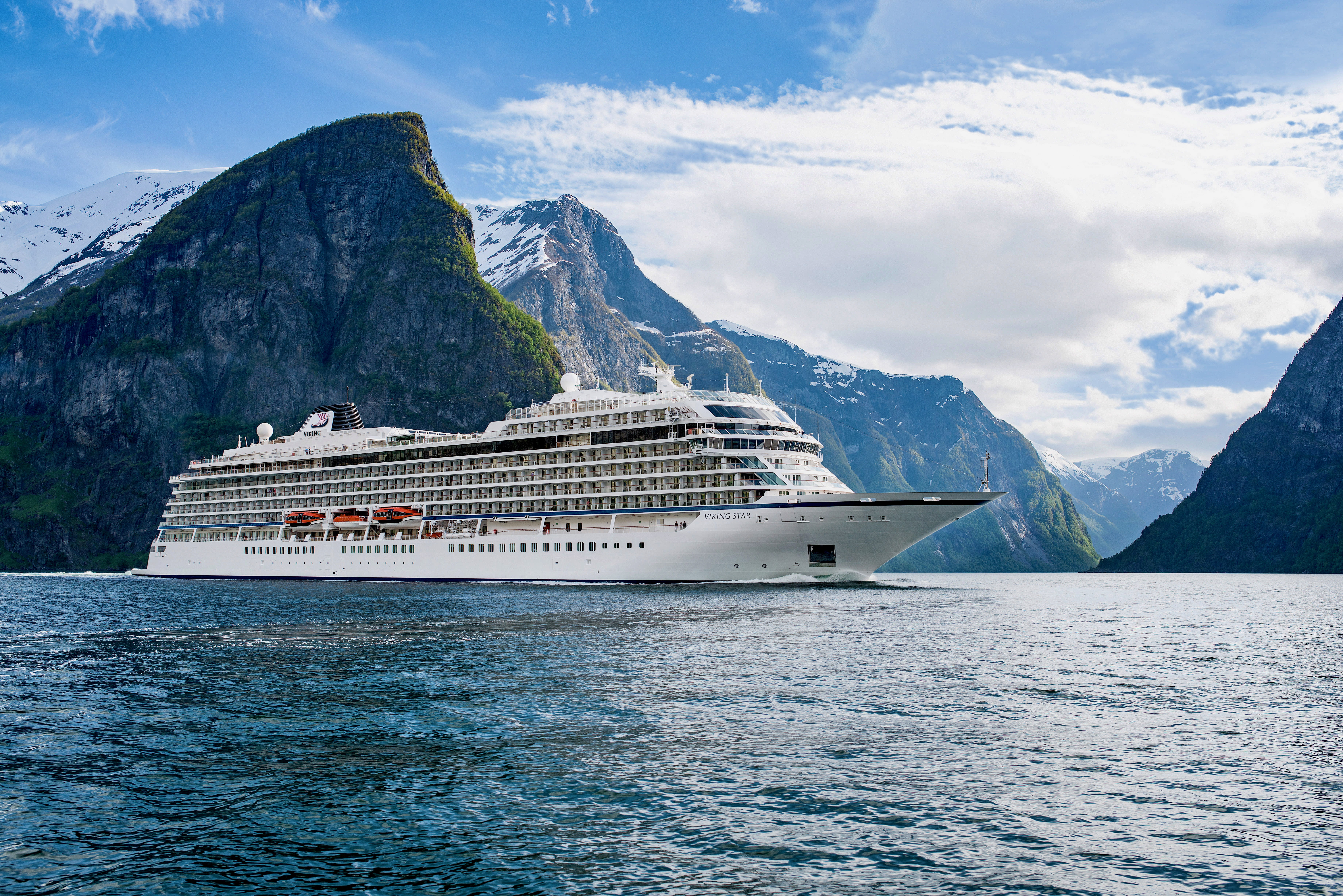 cruise ship at sea with towering mountains behind and blue skies
