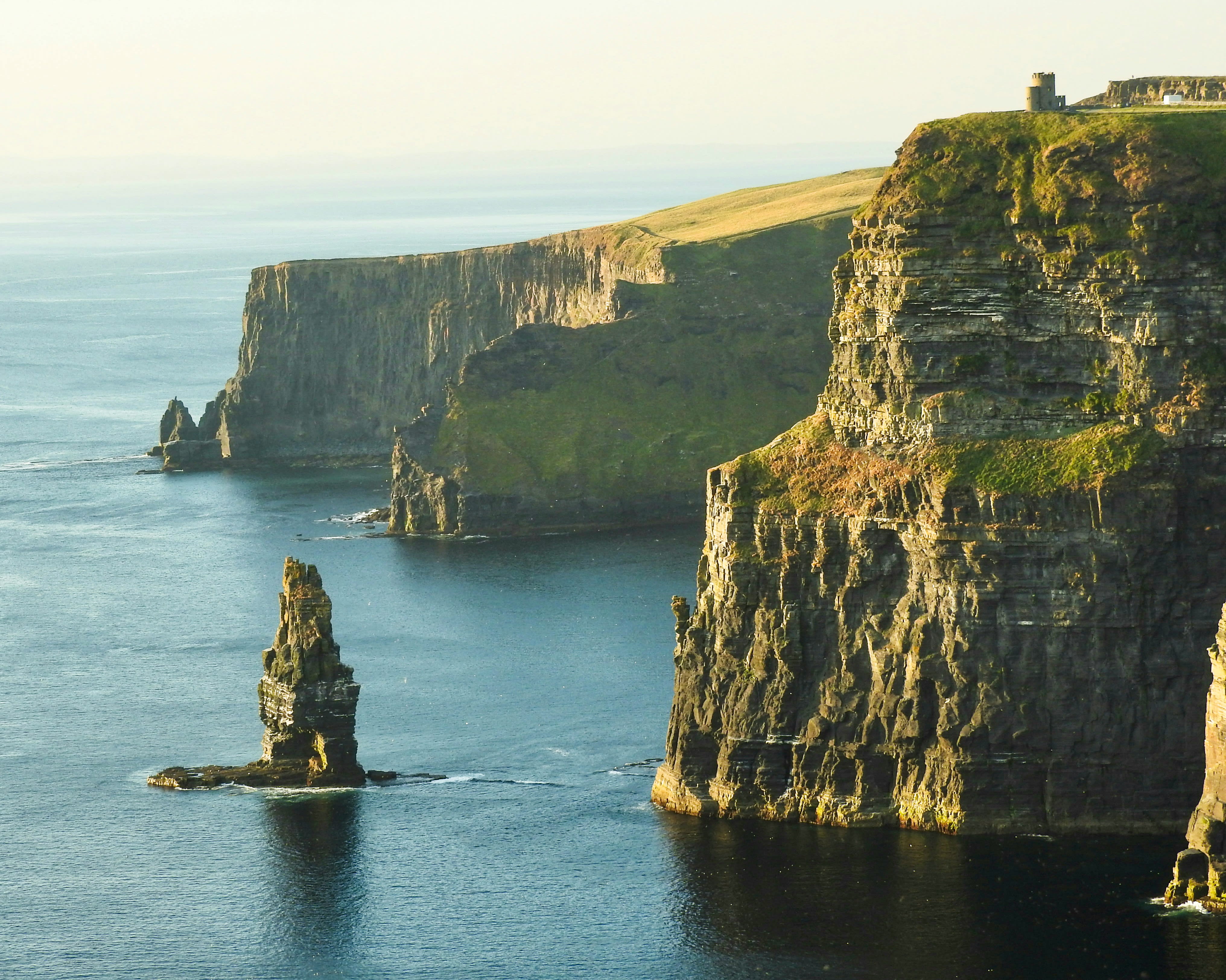 rock formation beside tall grass covered cliffs next to the sea at daytime